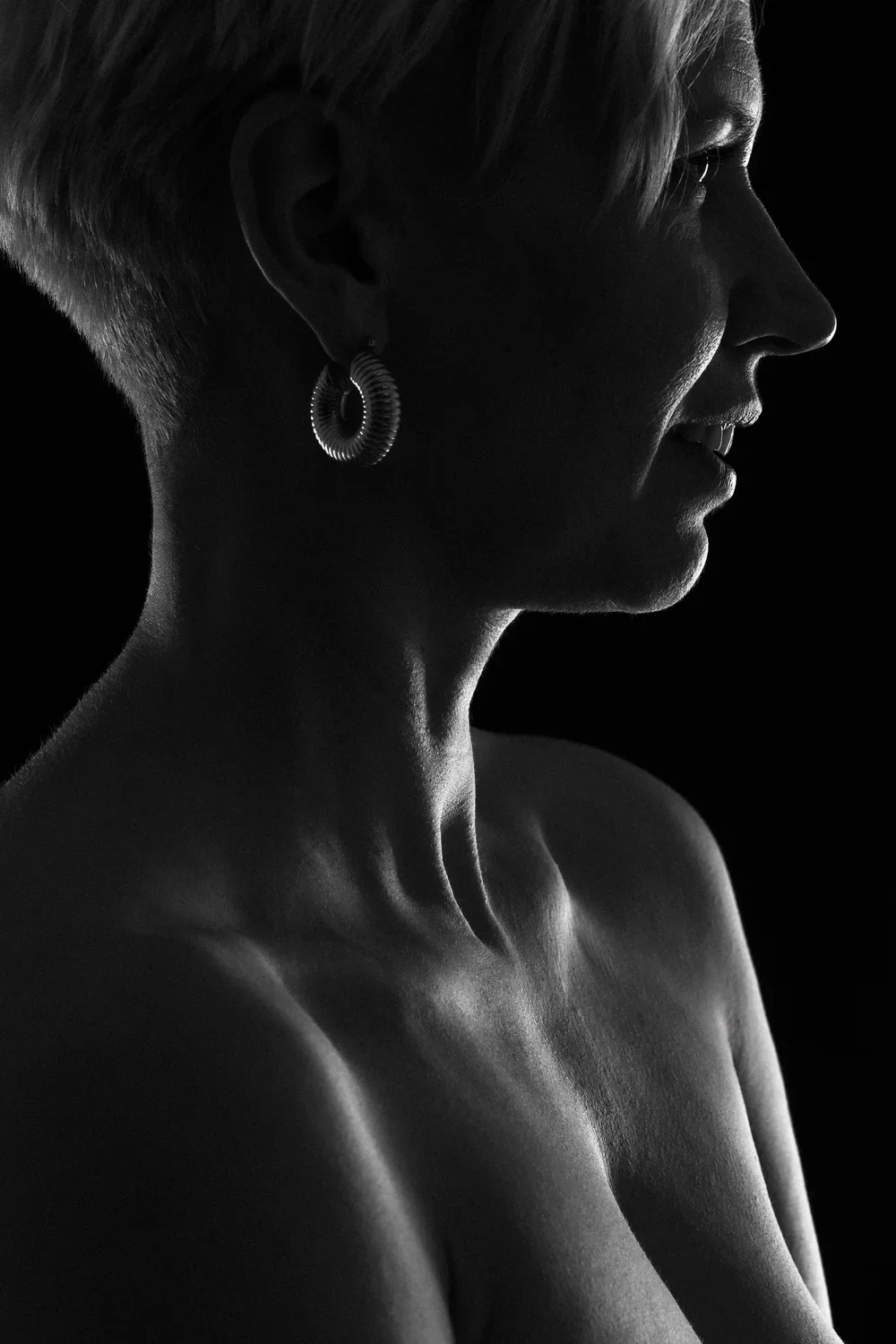 Silhouette of a woman with short hair, wearing hoop earrings, in side profile against a black background.