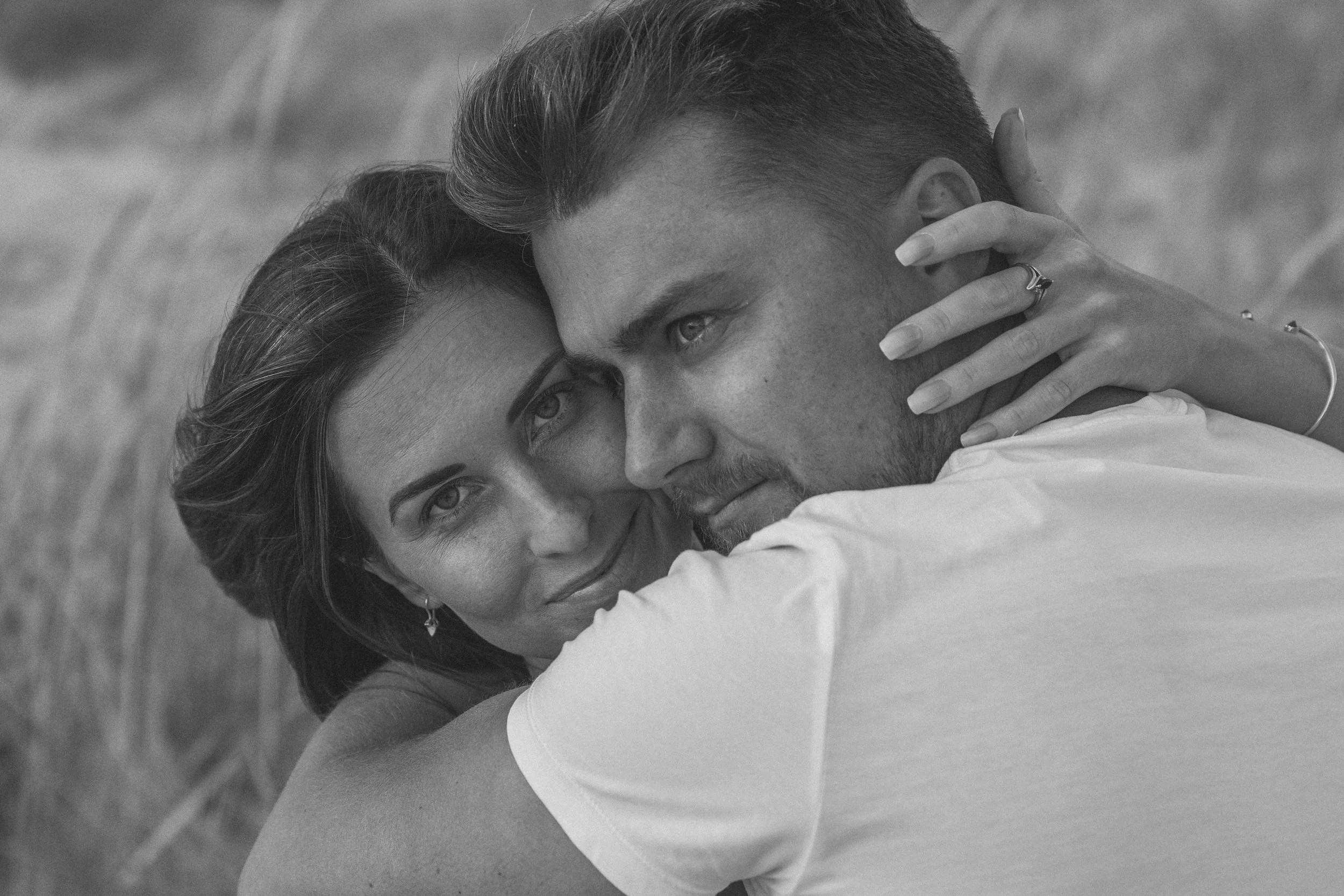 A black and white photo of a couple embracing closely, with the woman smiling and the man gently touching her face.