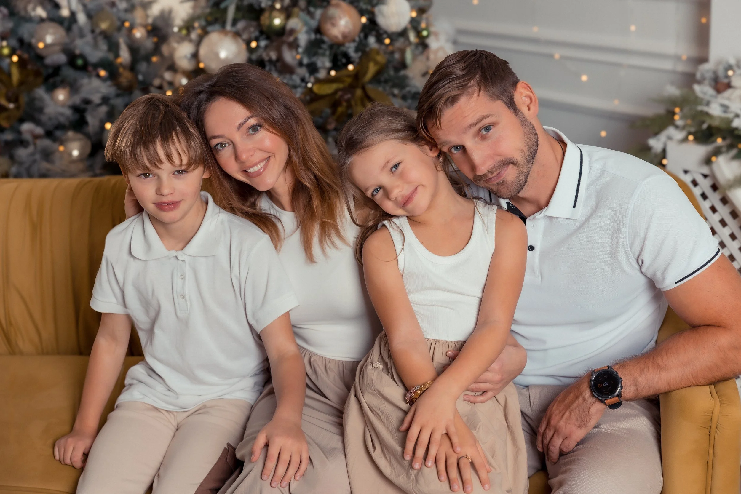 A family of five sitting on a green couch in front of a decorated Christmas tree, smiling at the camera.
