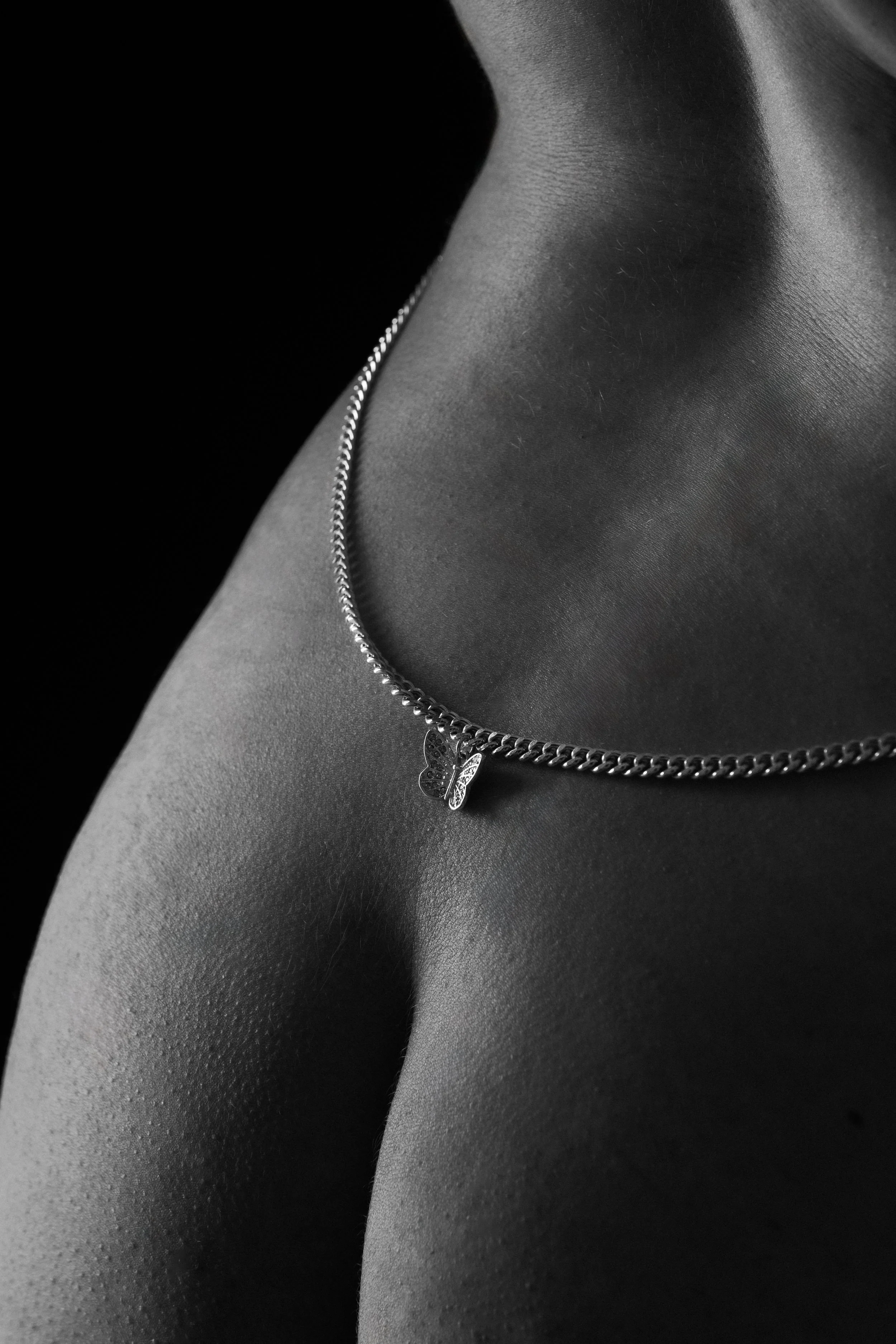 A close-up of a person's body, wearing a necklace with a butterfly pendant, with smooth, textured skin visible across the frame.