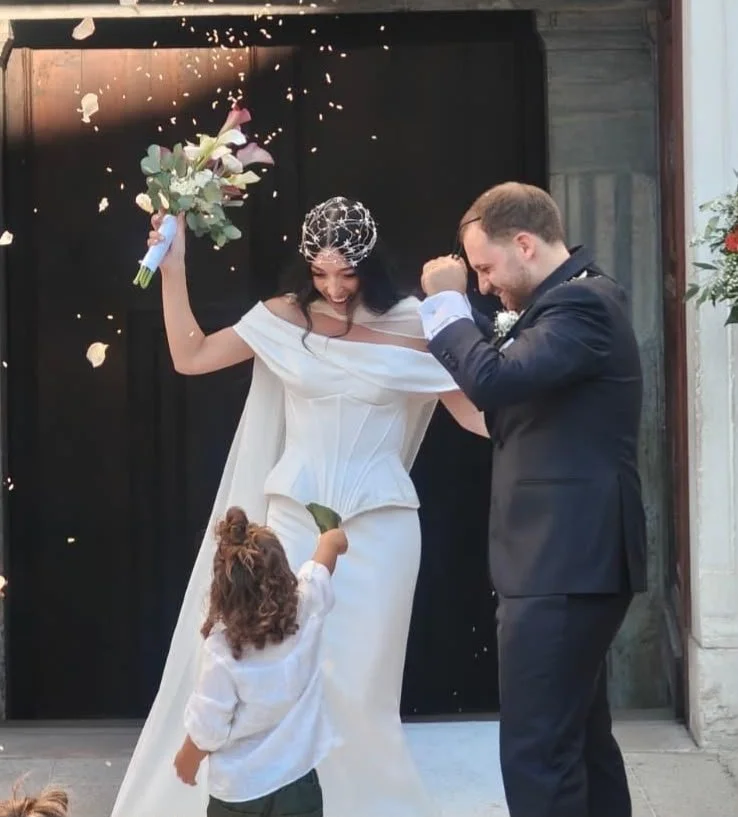 Una coppia di sposi felici, insieme a una bambina, festeggia all'esterno di una chiesa, con petardi che sprigionano scintille per celebrare il matrimonio.