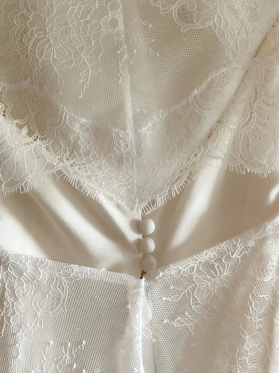 Particolare di un abito da matrimonio o abito elegante con dettagli di pizzo bianco e bottoni stondati.