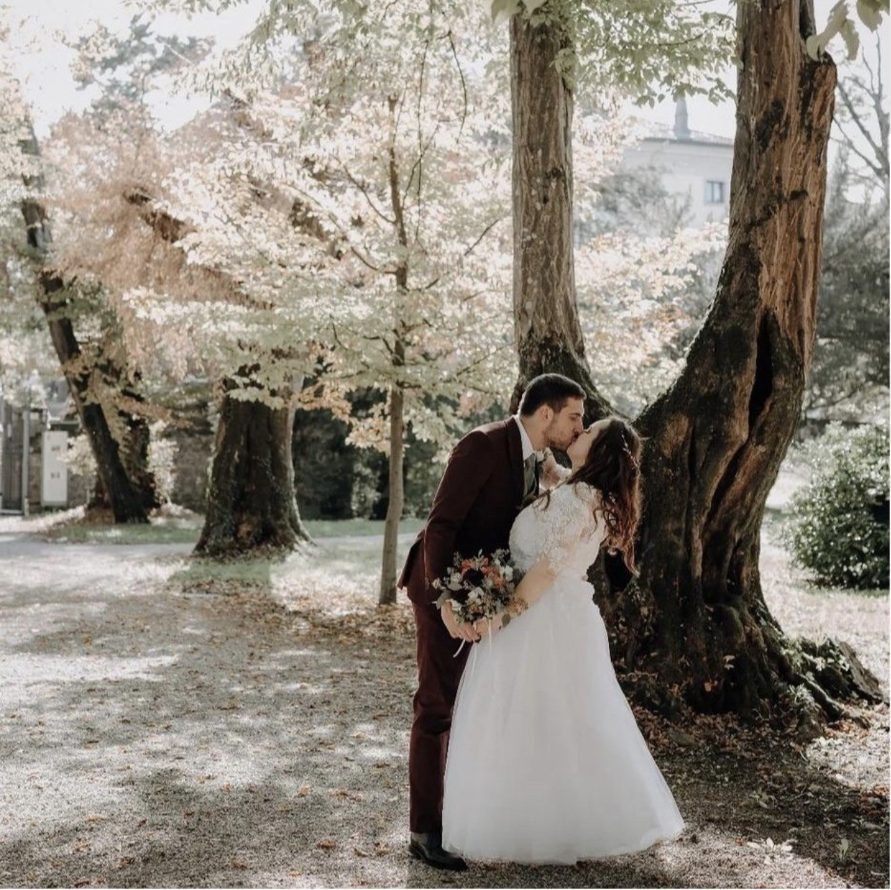 Una coppia di sposi si bacia sotto un albero in fiore durante uno scatto matrimoniale in un parco.