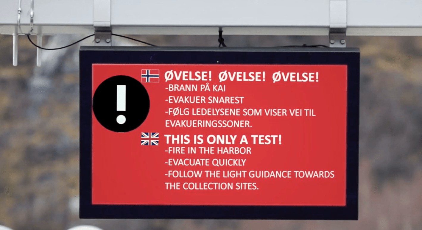 Varselskilt med informasjon om øvelse, inkludert brann, evakuering og ledelys, med norske og engelske instruksjoner.