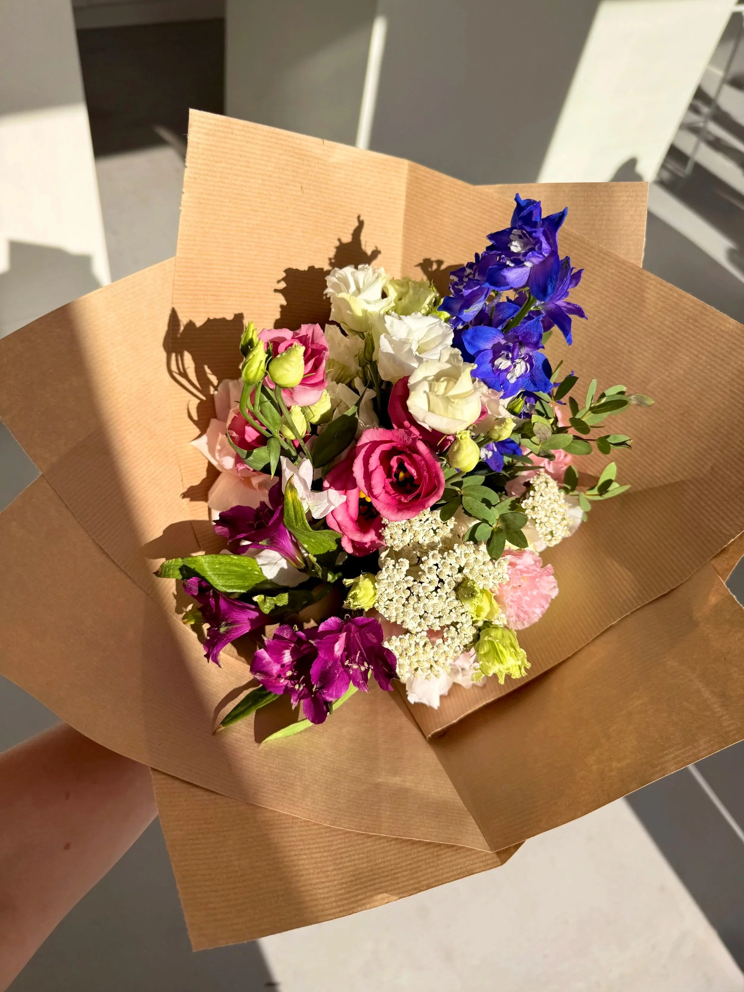 A bouquet of mixed colorful flowers wrapped in brown paper.