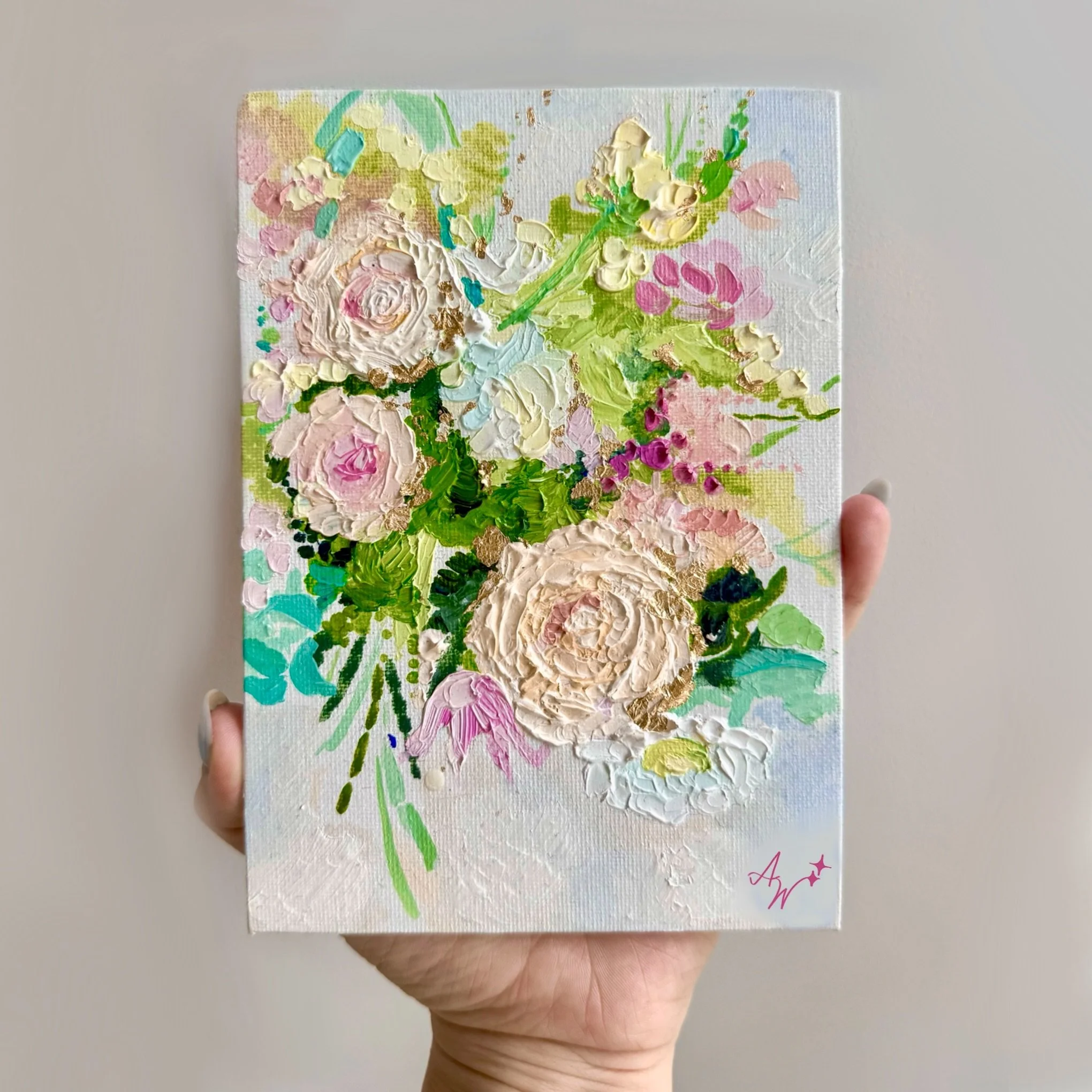 A small abstract floral painting with pink, white, green, and hints of blue and gold acrylic paint, held in a person's hand against a plain background.