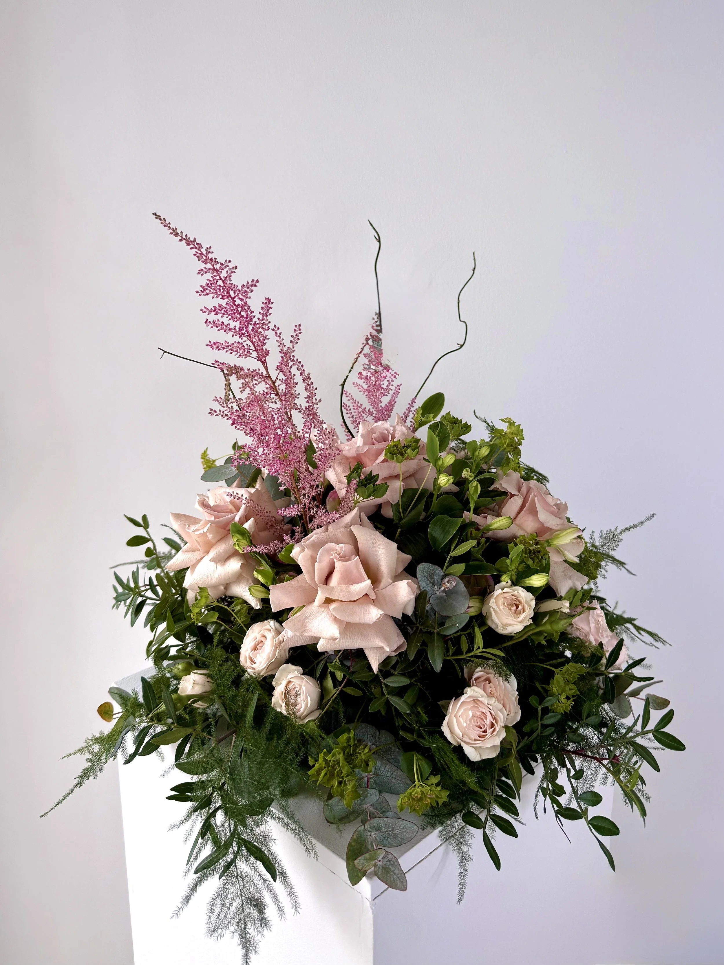 A floral arrangement with light pink roses, pink astilbe, green leaves, and sprigs of eucalyptus.