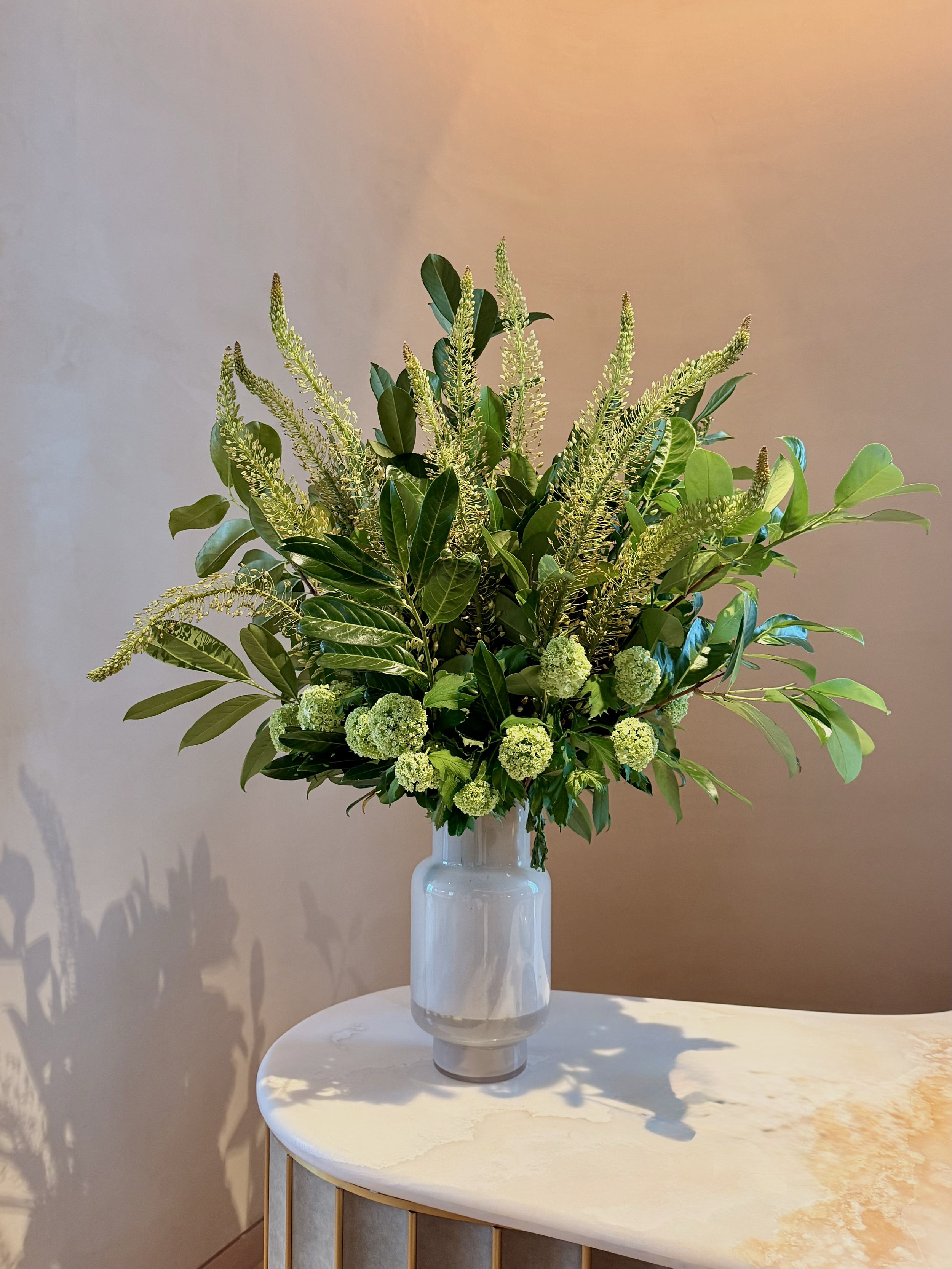 A large bouquet of green flowers and foliage arranged in a white vase on a round white table.