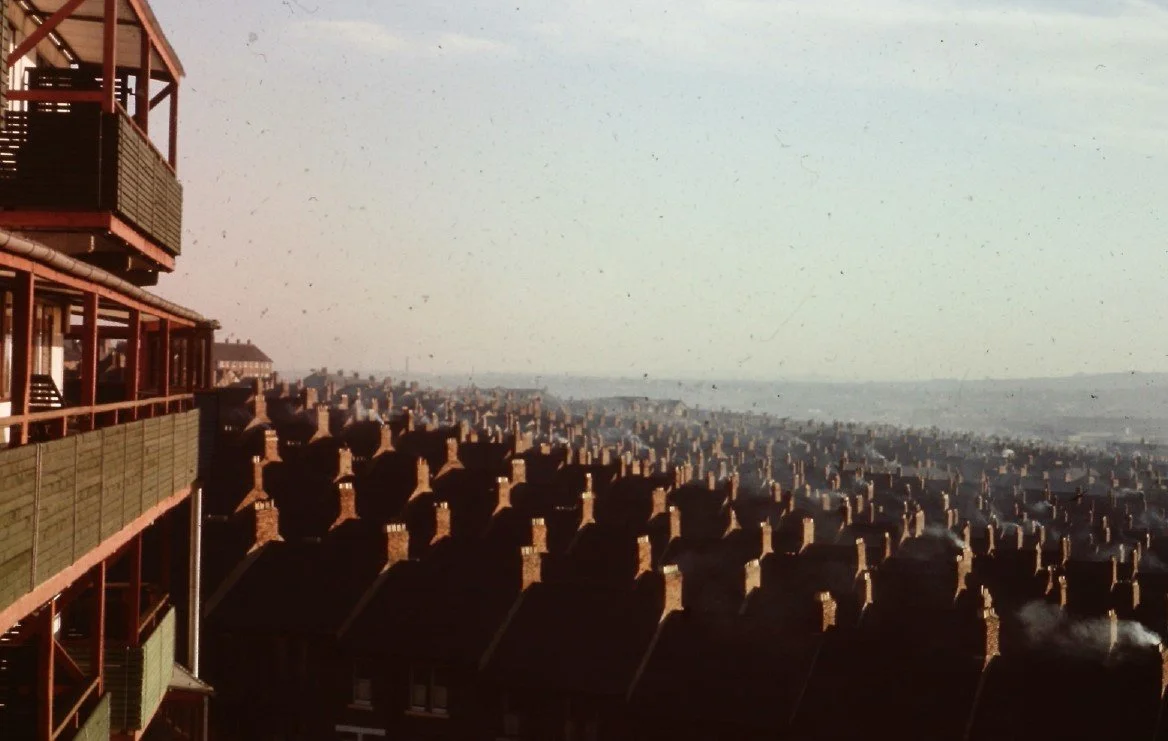 Faded colour photograph showing green and red Byker Wall balconies overlooking old Byker terraced housing sloping down towards the River Tyne
