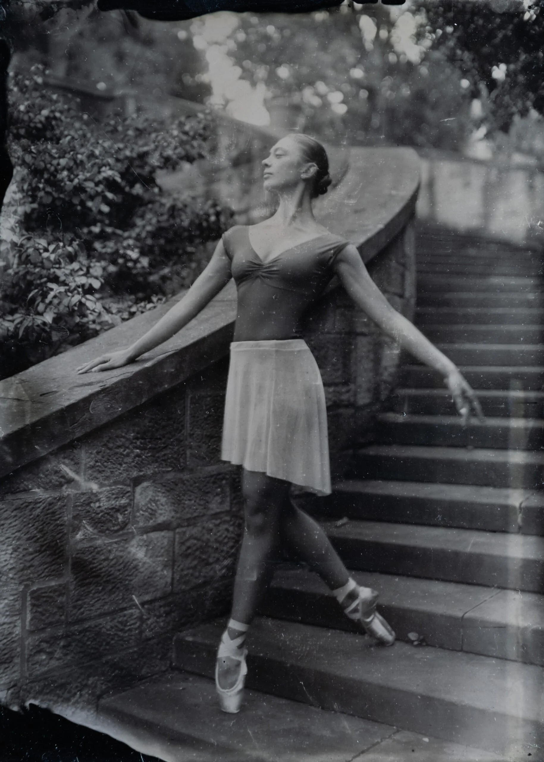 A ballet dancer in a tutu and ballet shoes posed on a staircase outdoors.