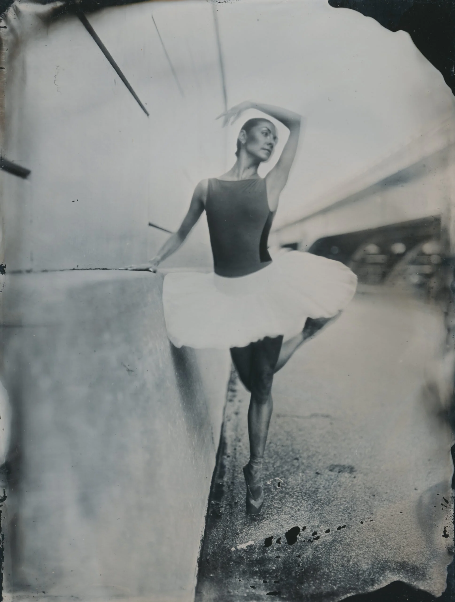 A ballerina dressed in a leotard practicing ballet in a dance studio, seen through an artistic, monochrome, torn paper frame.