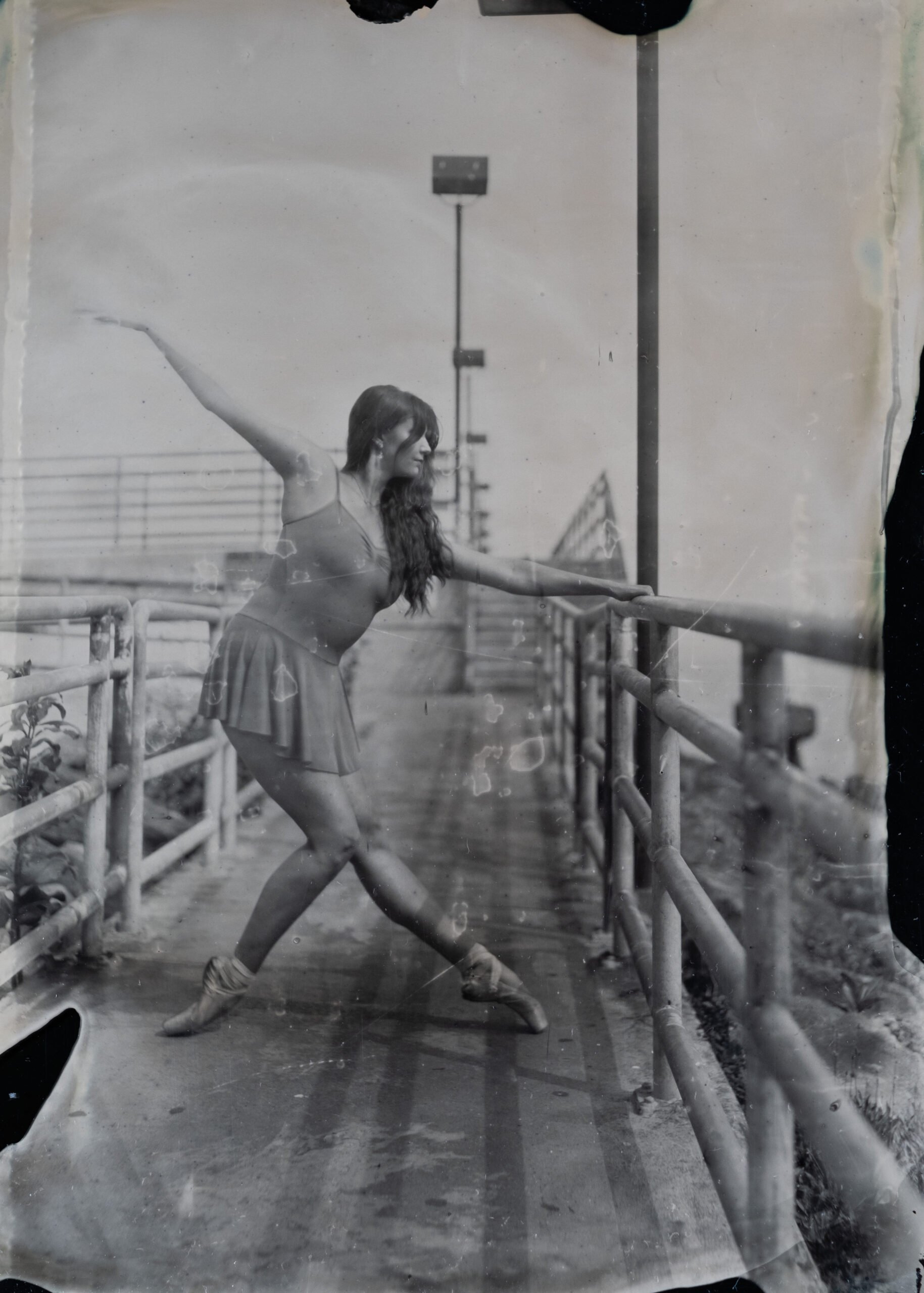 A woman practicing ballet in an outdoor dance studio with railings and a cityscape background.
