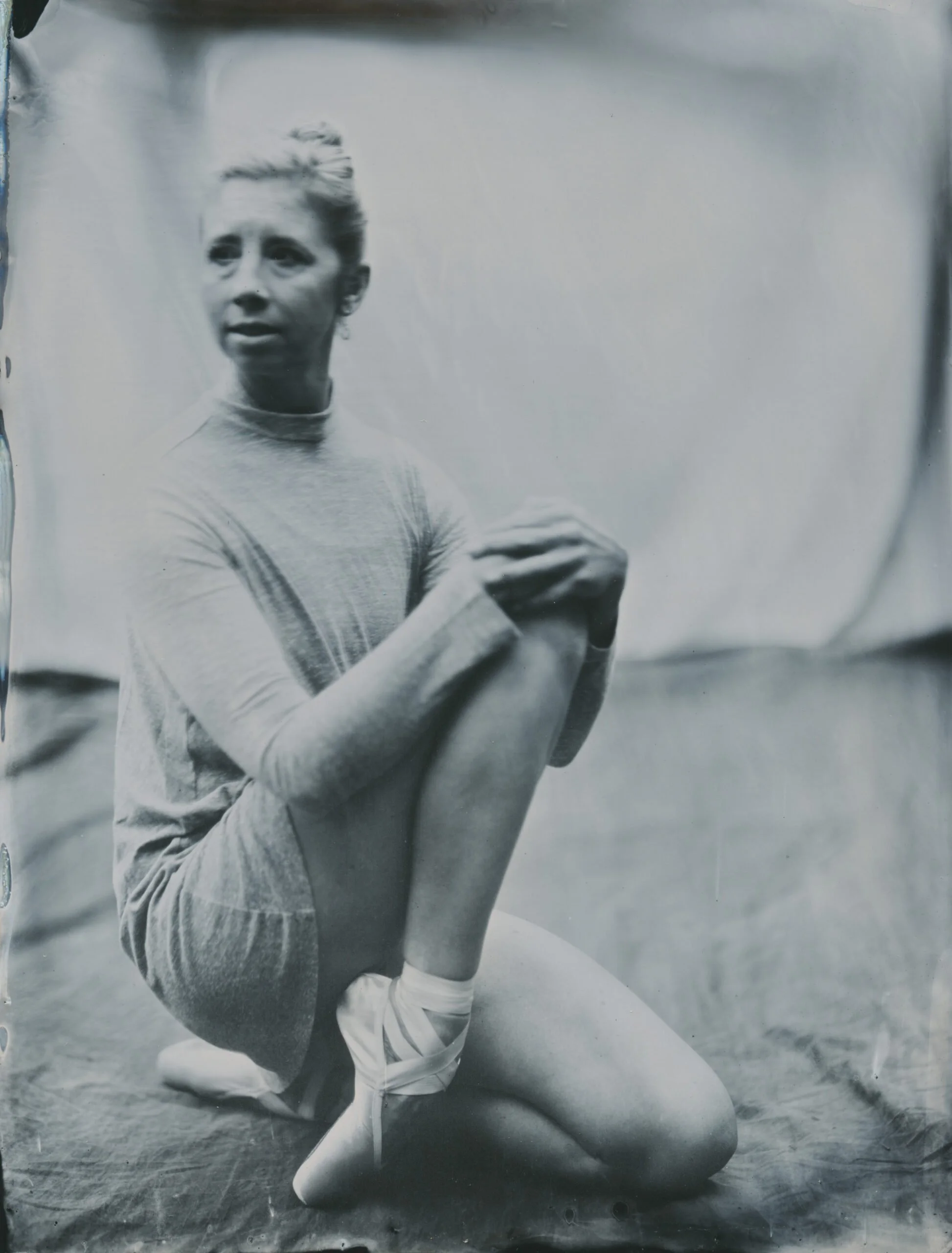 A woman doing yoga outdoors in a cross-legged position, wearing a light-colored long-sleeve shirt and pants, on the grass.