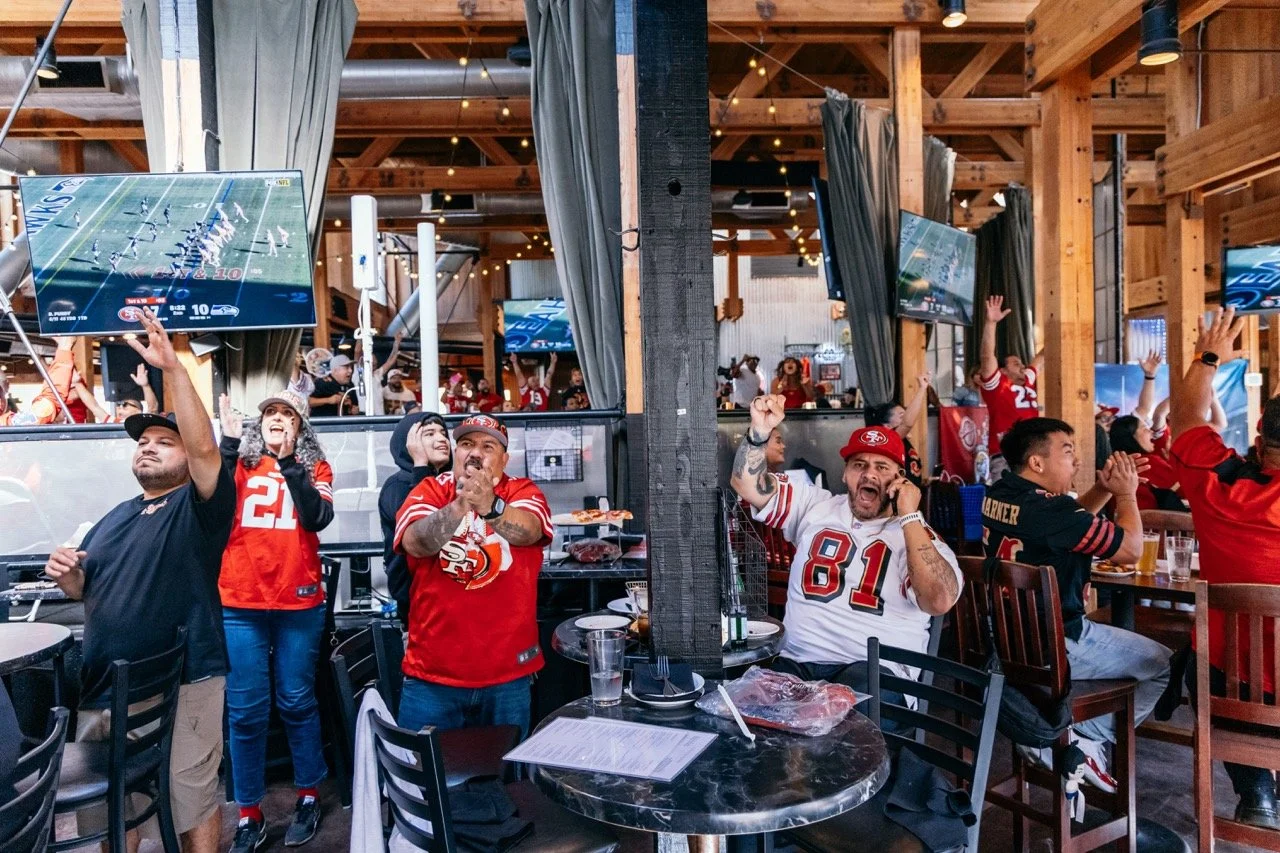 San Francisco 49ers football fans watching a game at a bar or restaurant, cheering and celebrating.