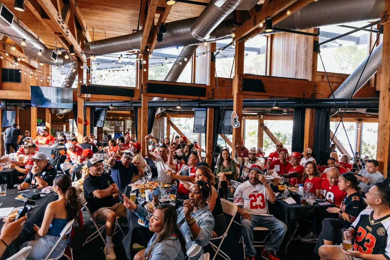 People watching a sports game on multiple screens in a wooden-finished restaurant or bar decorated with string lights.