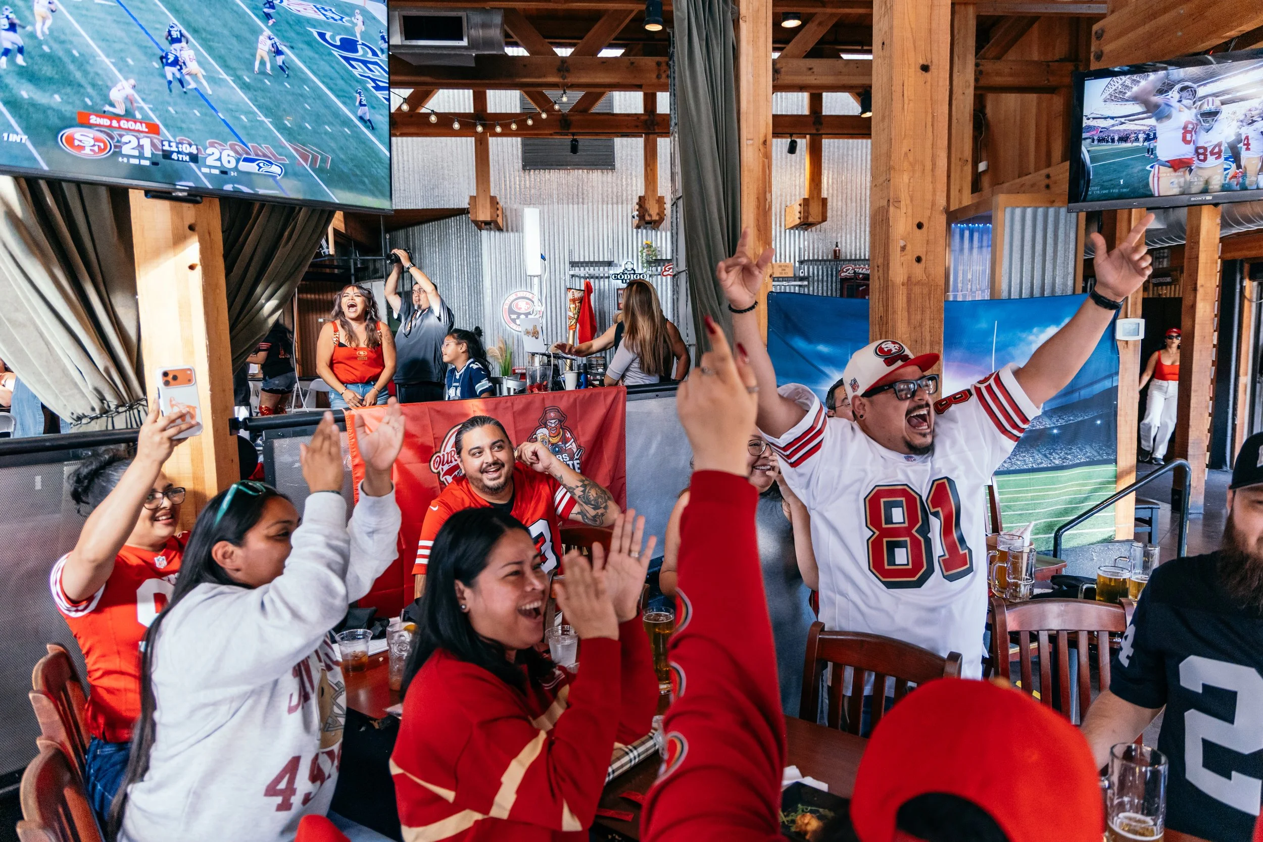 Football fans at a sports bar watching a game on multiple large screens, wearing team jerseys, cheering and celebrating.