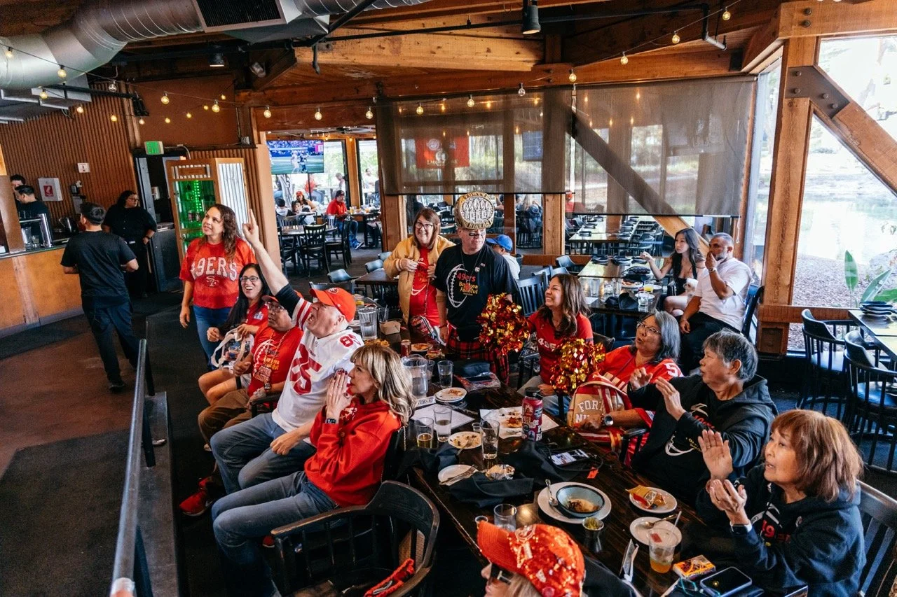 People gathered in a restaurant dressed in San Francisco 49ers football team apparel, celebrating together with food and drinks, likely a game day or special event.