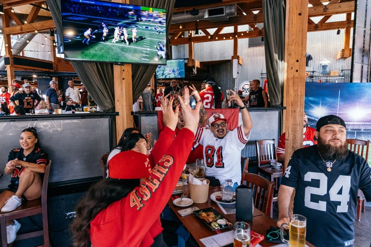 Group of San Francisco 49ers fans cheering and celebrating in a sports bar while watching a game on TV.