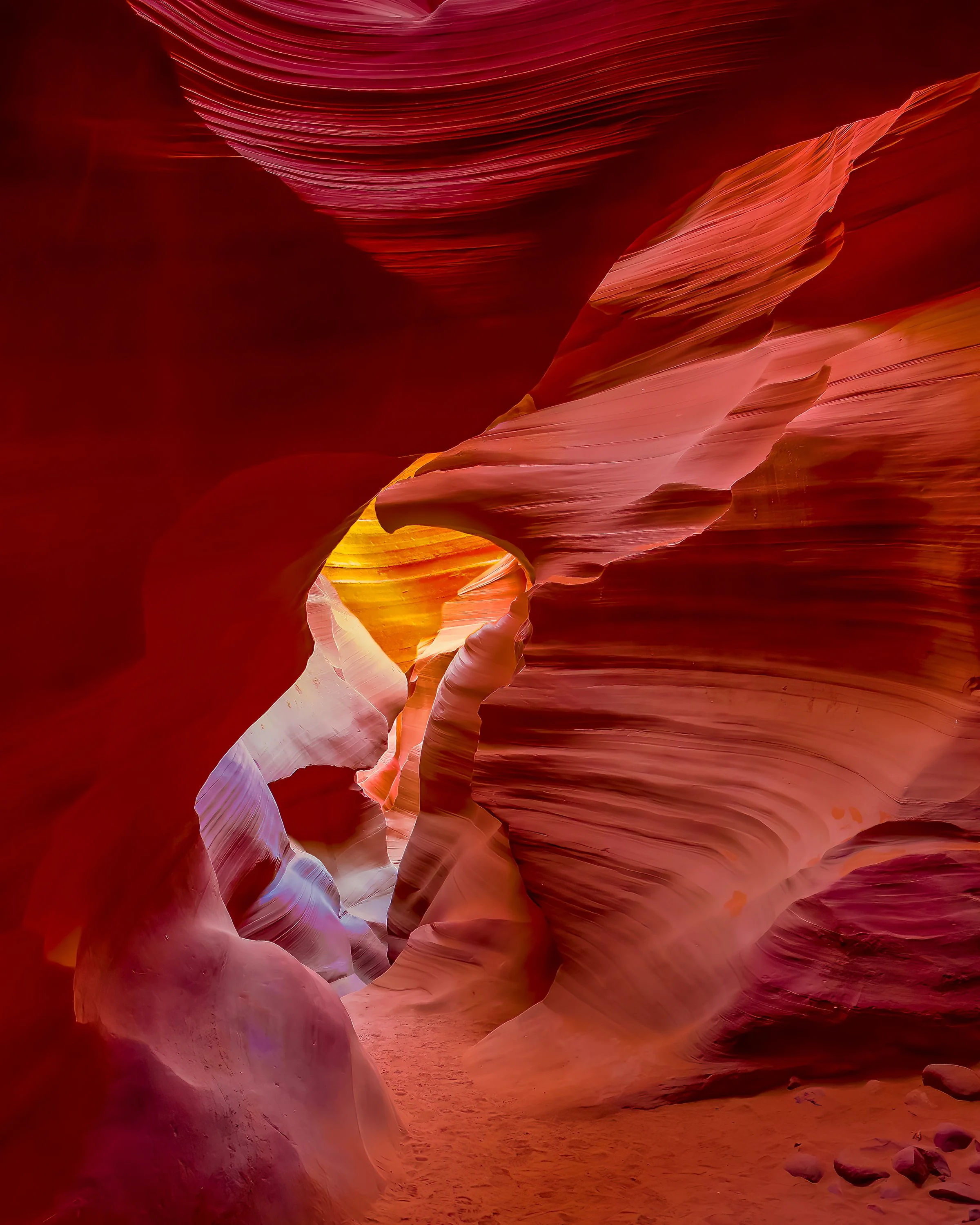 Narrow slot canyon interior with smooth, layered sandstone walls in red, orange, and yellow hues, with sunlight filtering through the opening.