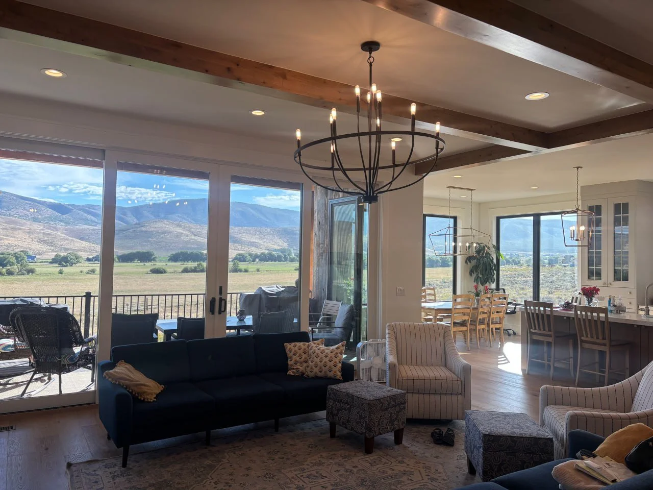 Living room with large windows showcasing a mountain view, modern furniture including a navy sofa with pillows, striped armchairs, and a chandelier.