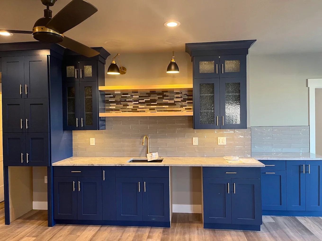 Modern kitchen with blue cabinets, marble countertop, gray subway tile backsplash, and decorative tile accent with lighting above.
