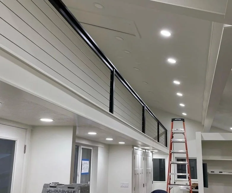 Interior of a modern house showing a loft with a black railing, recessed ceiling lights, and a red ladder.