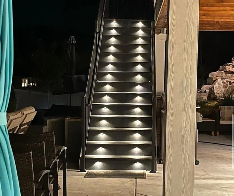 Outdoor staircase with built-in lights at night, leading upstairs in a modern deck area with outdoor seating and rocks in the background.