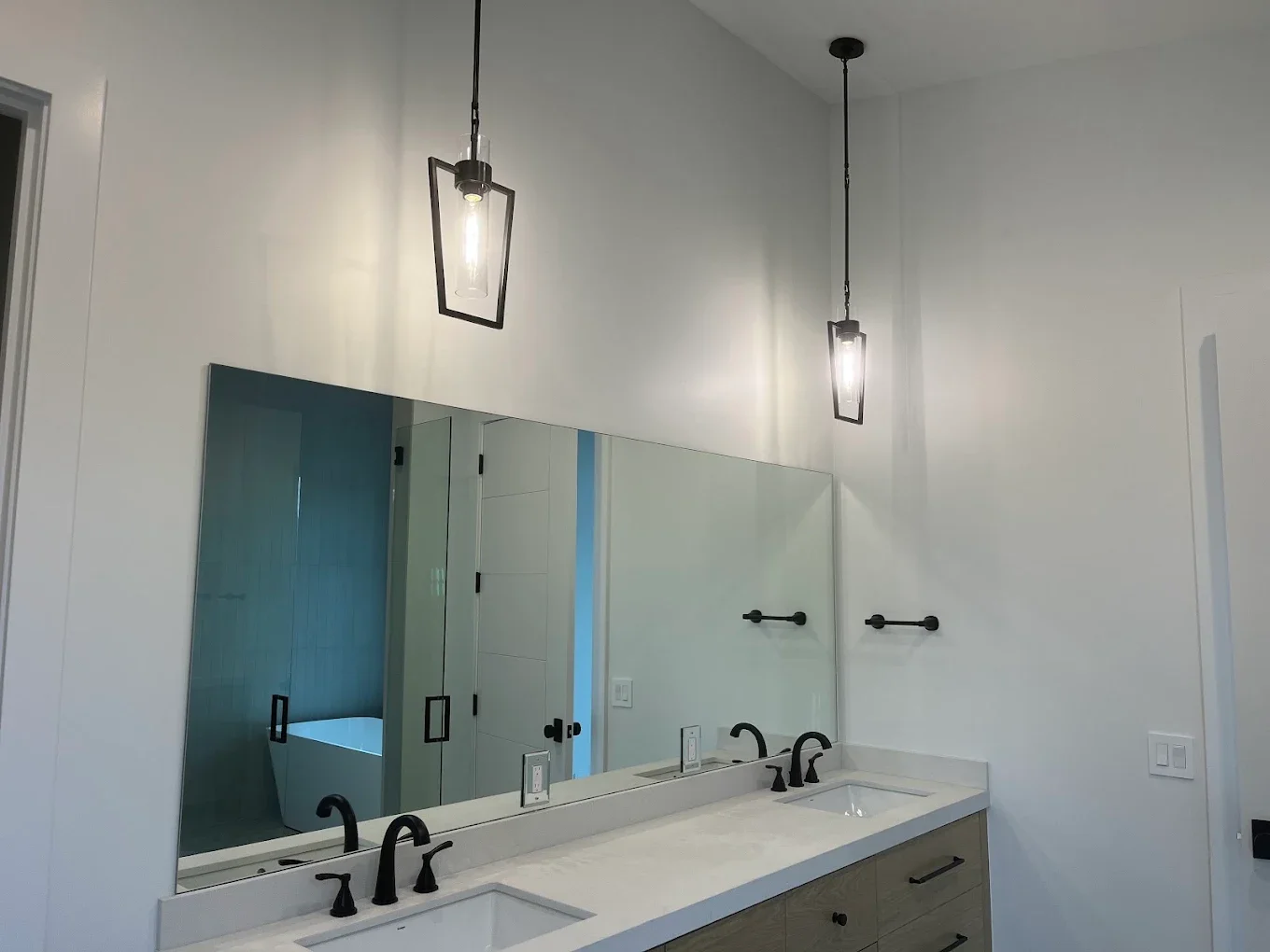 Modern bathroom with dual sinks, white countertop, black fixtures, large mirror, and pendant lights.