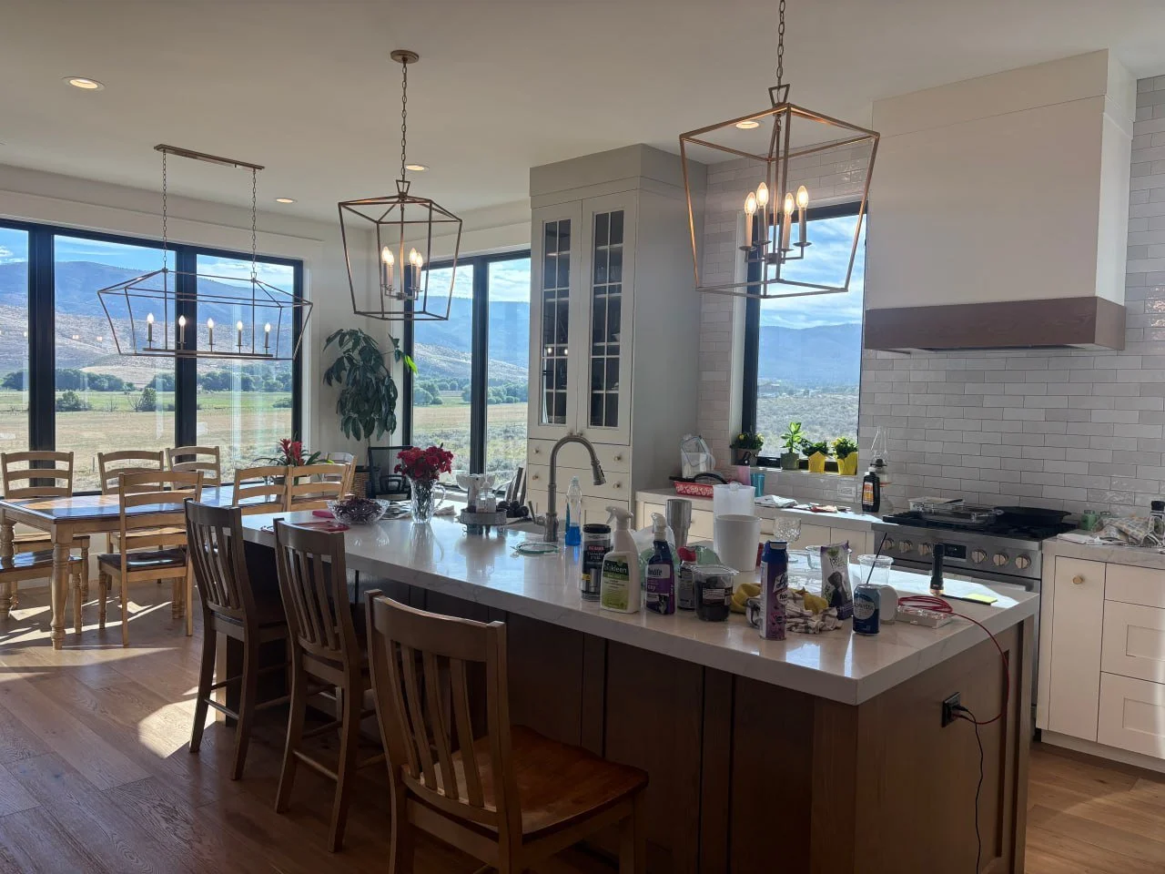 Modern kitchen with large island, hanging geometric light fixtures, white cabinets, and a view of mountains through large windows.