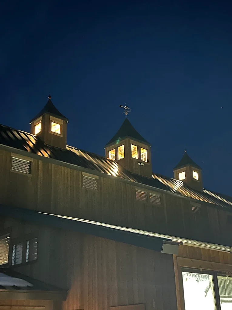 Night view of a large wooden building with three lit towers topped with small spires, set against a dark sky with a bright star or planet visible, and a faint crescent moon.