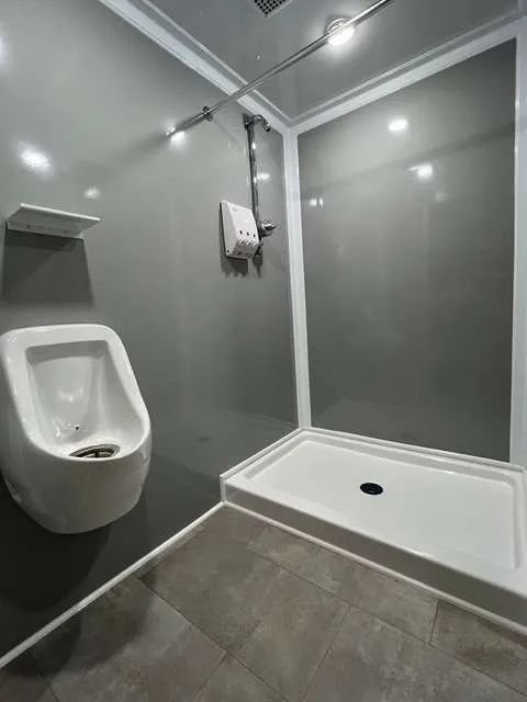 Accessible bathroom with a urinal, a shower with a drain, and a hand-held shower head on a gray wall.