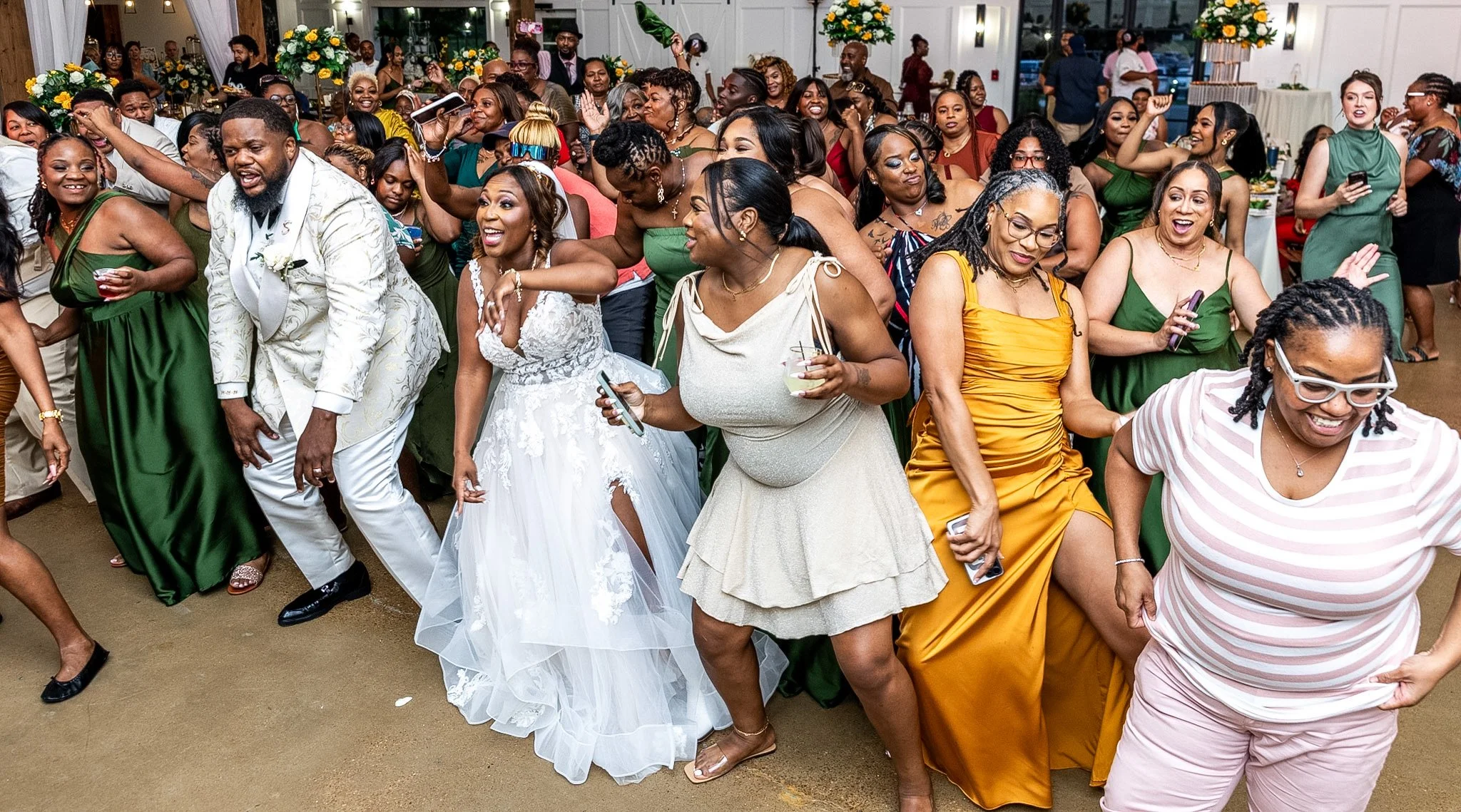 Guests dancing and celebrating at a wedding reception, with floral centerpieces and a festive atmosphere.