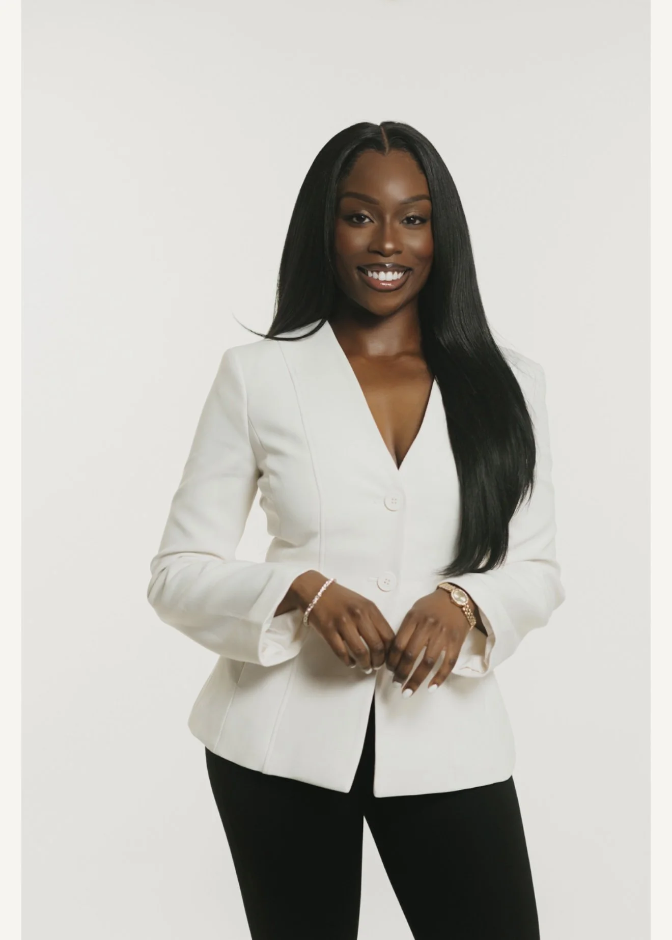 Hawa Swaray wearing a white blazer and black pants standing against a plain white background, smiling at the camera for Keita Beauty in Halifax Nova Scotia Canada for skincare, facial, and beauty services.