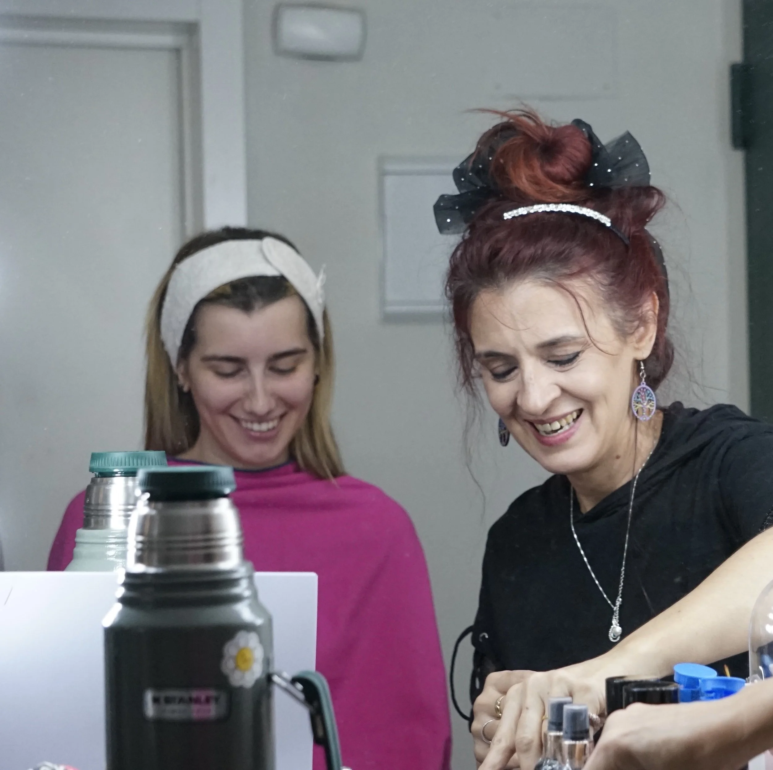 Dos mujeres en un laboratorio manipulan frascos y tubos de ensayo, una de ellas con cabello rojo y otro moreno, ambas parecen concentradas en su trabajo.