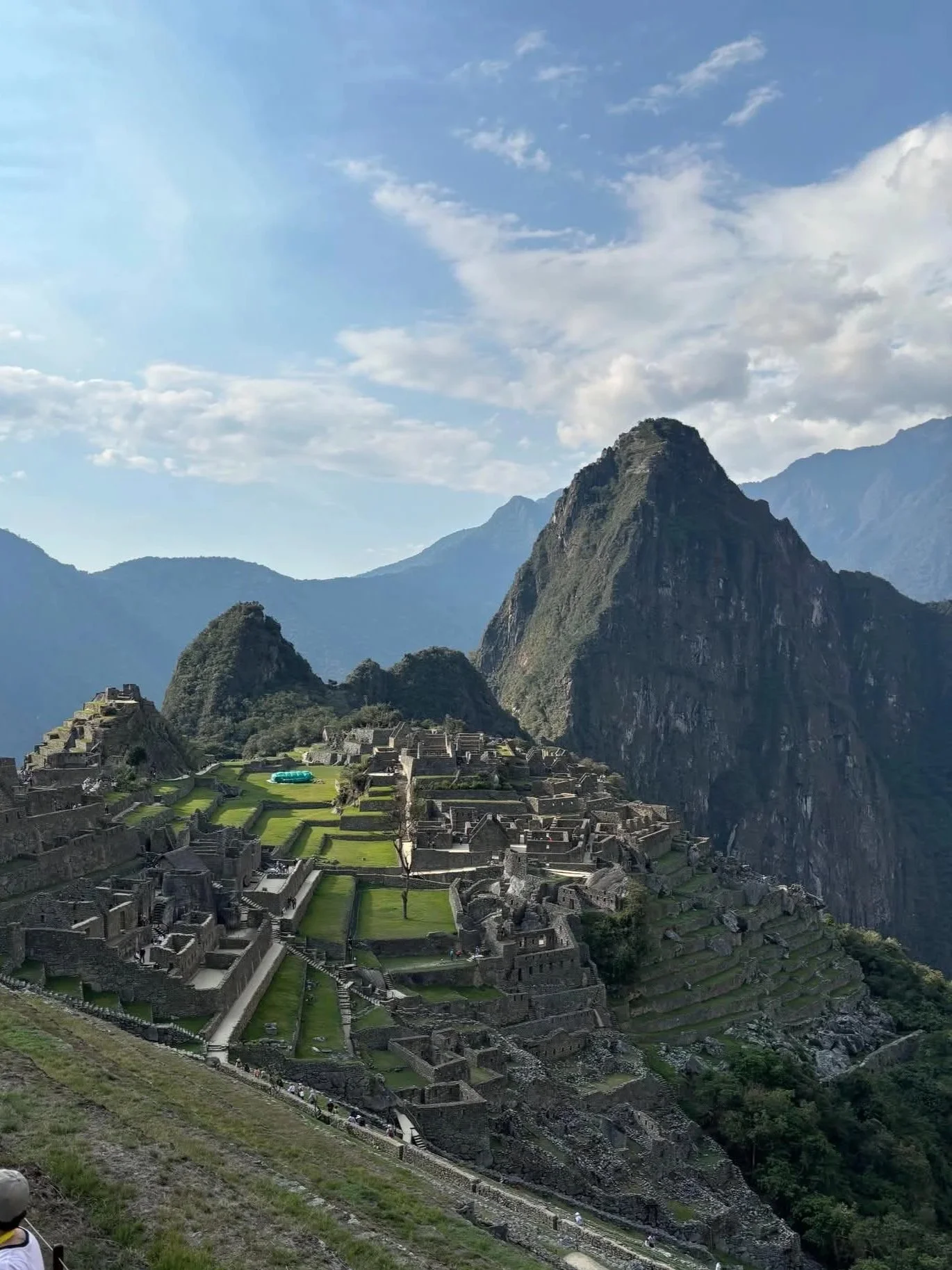 Ancient Incan ruins at Machu Picchu with terraced fields, stone structures, and surrounding mountains under a blue sky with clouds.