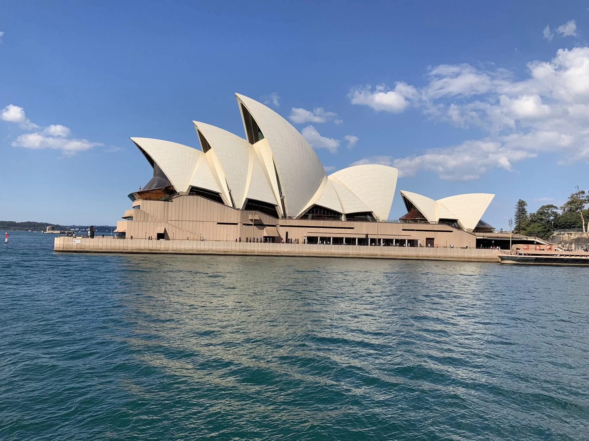 Sydney Opera House with blue sky and water in foreground.