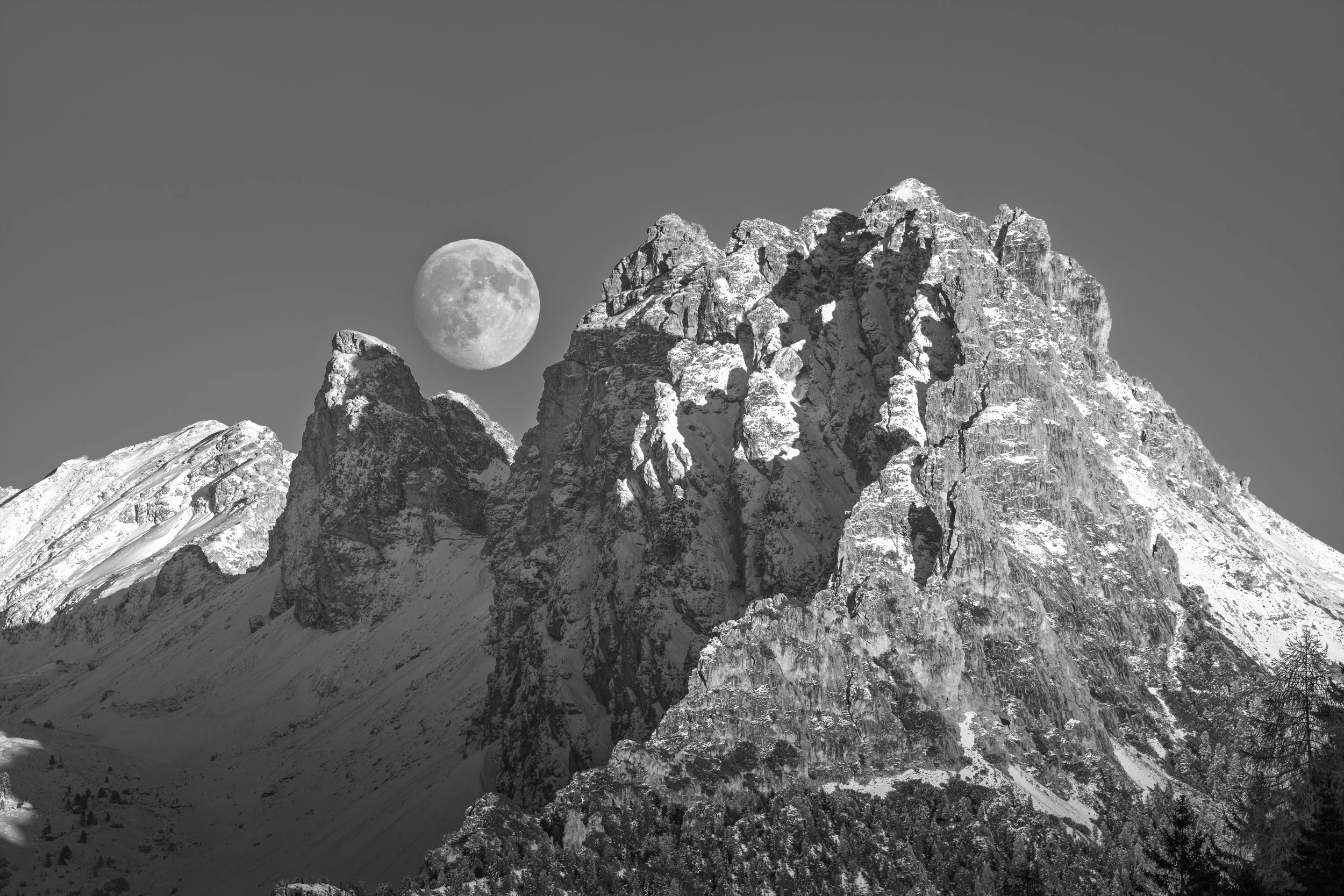 Schneebedeckte Berggipfel bei Nacht mit Vollmond am Himmel.