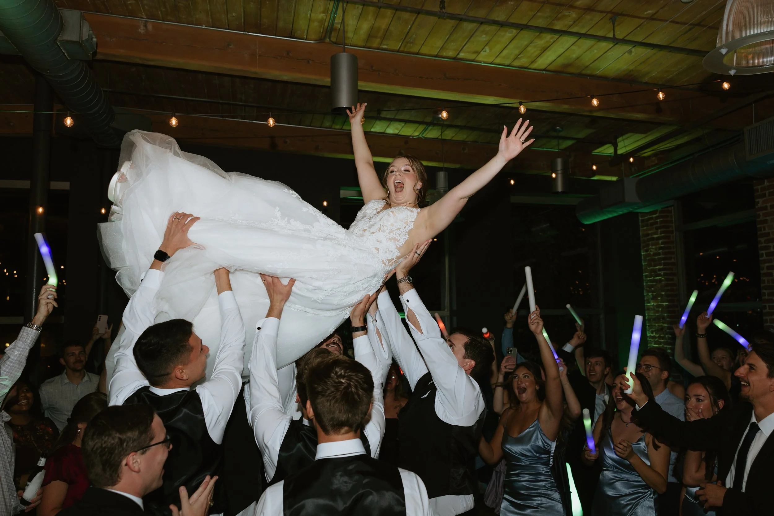 A bride in a white dress is in the air at Huguenot Loft in Downtown Greenville SC as their wedding DJ plays music.