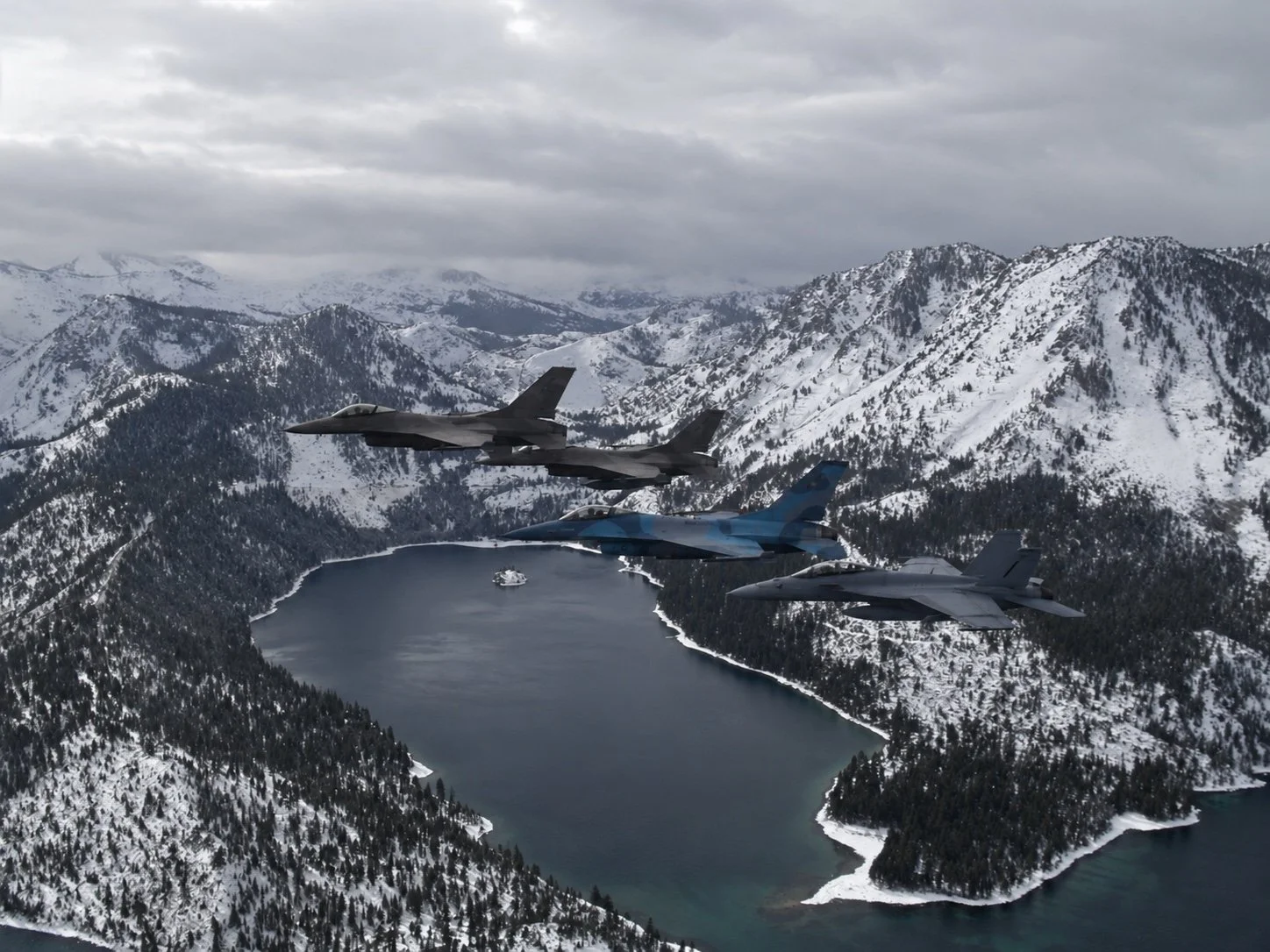 Military aircraft flying over snowy mountains and a lake
