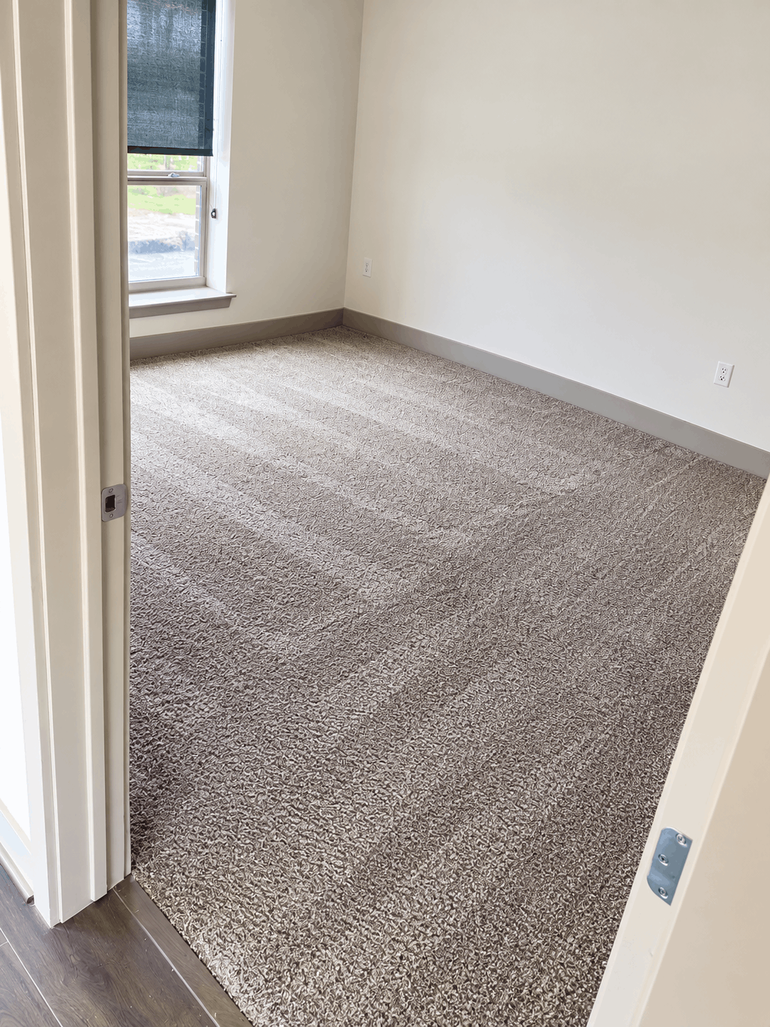 Empty room with beige carpet, white walls, a window with a dark shade, and electrical outlets.
