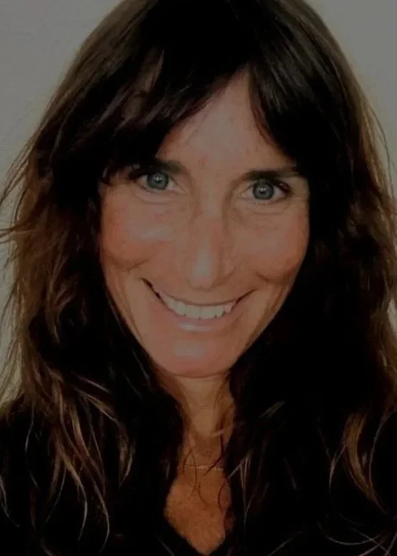A woman with long, wavy brown hair and blue eyes smiling at the camera.