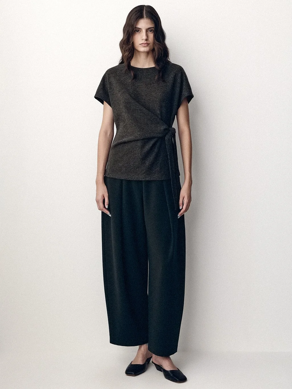 Woman in a dark short-sleeved top and wide black trousers standing in the studio.