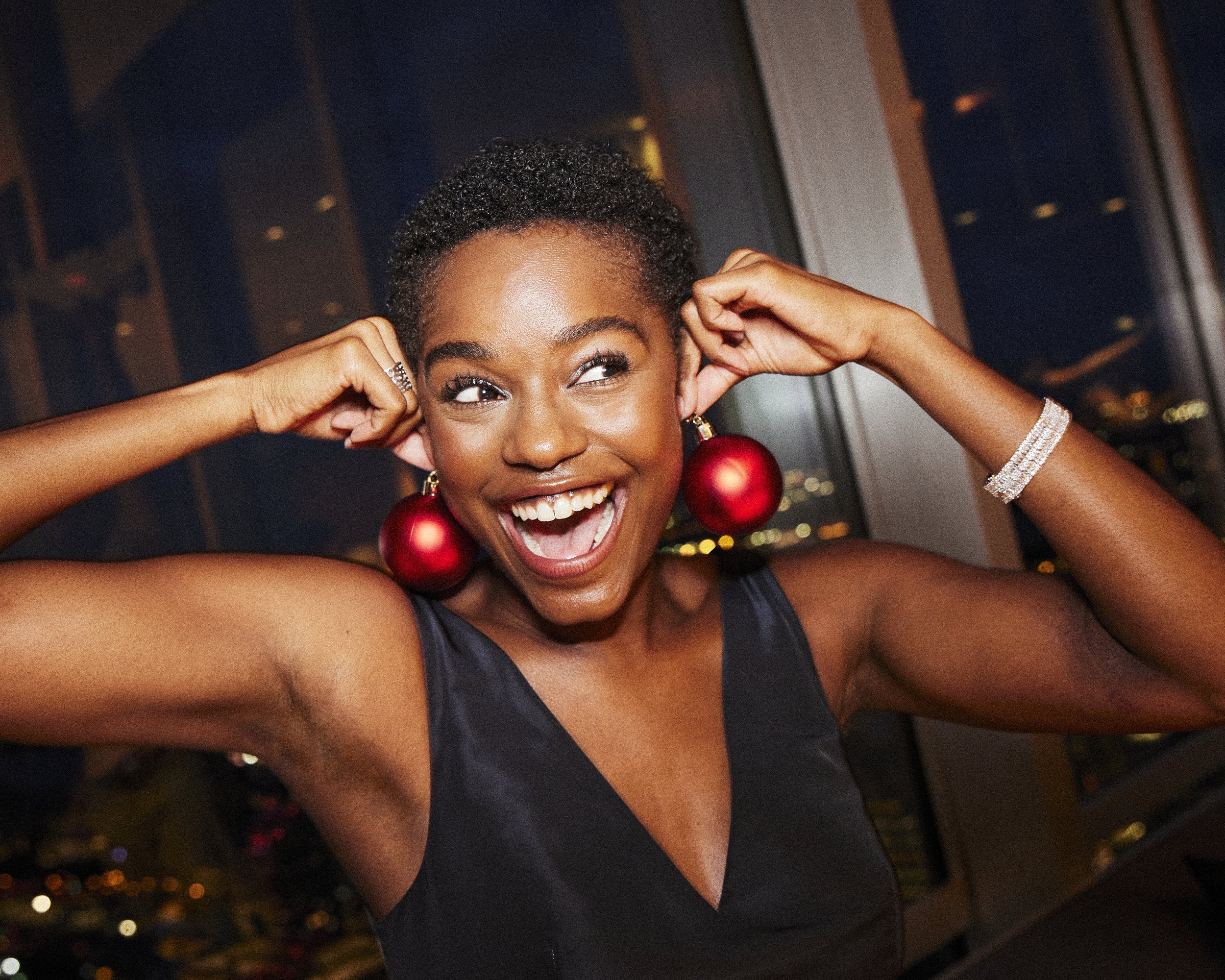 Woman laughing while holding red Christmas ornaments beside her ears.