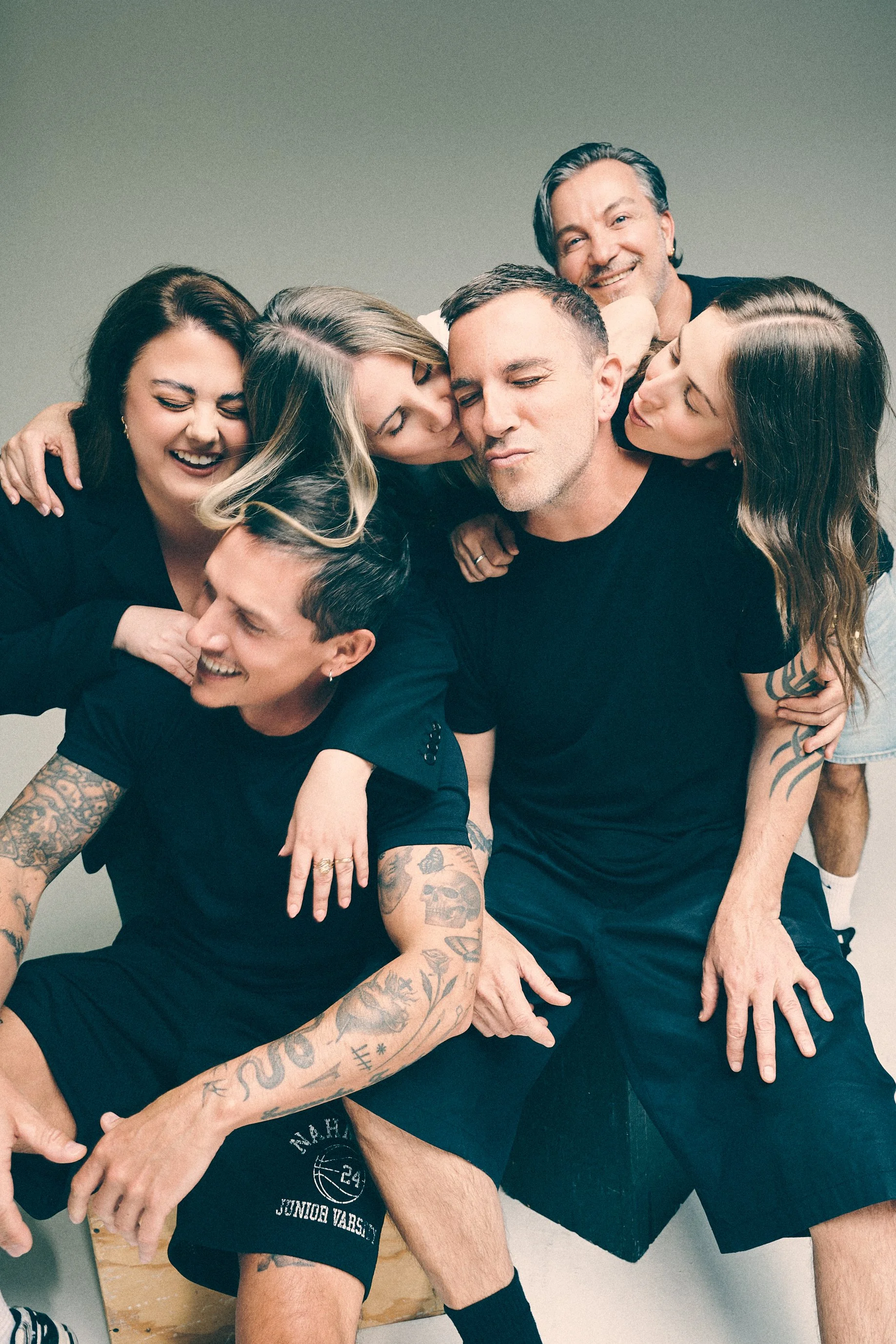 Playful group portrait of six people laughing and leaning together around two seated men.