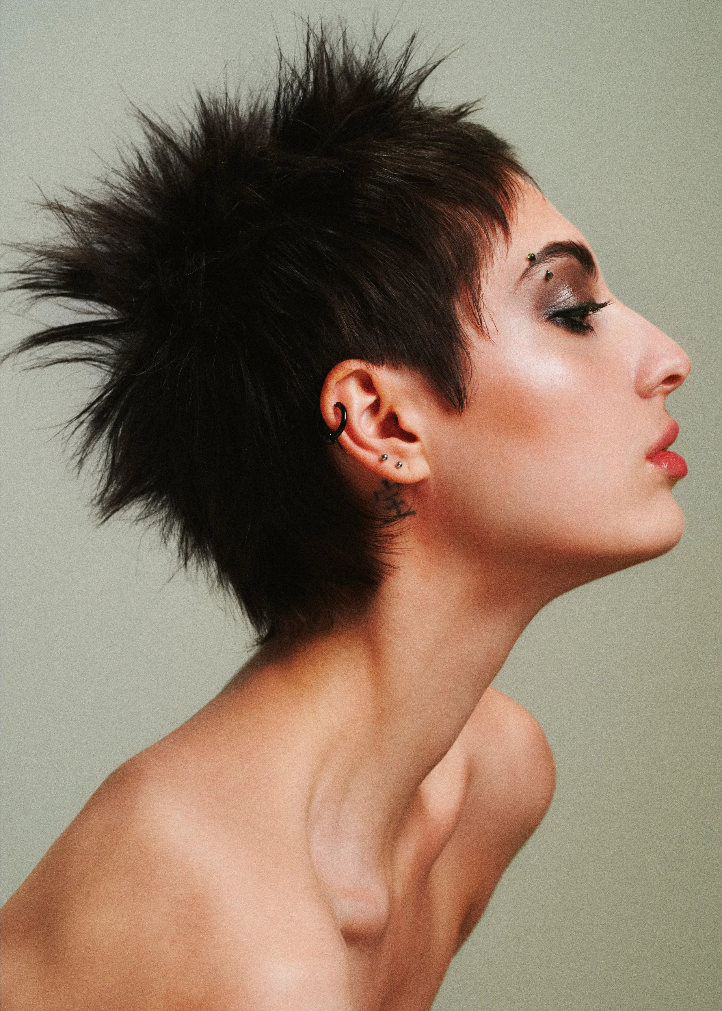 Side-profile beauty portrait with short spiked black hair and smoky eye makeup.