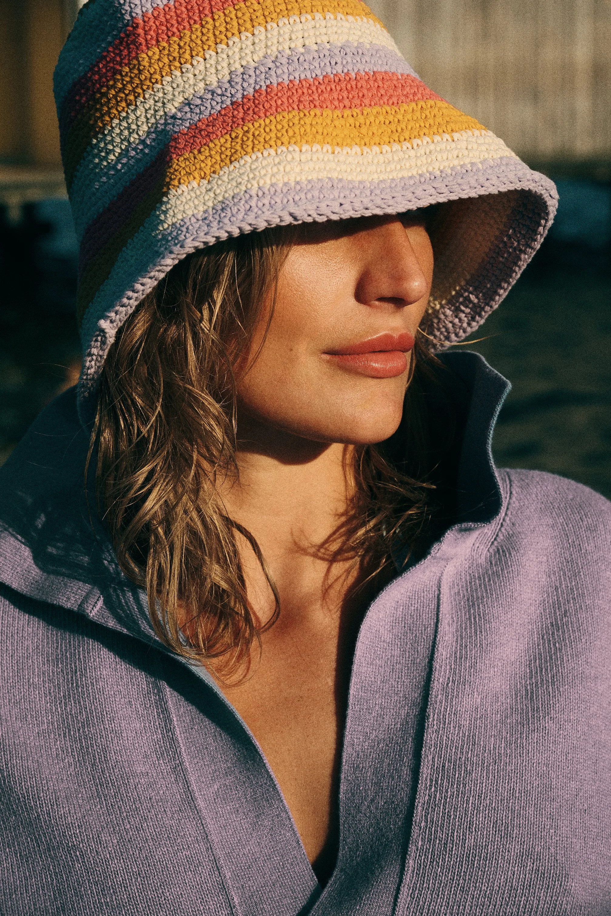 Close portrait of a woman in a colourful knitted bucket hat and lavender top.