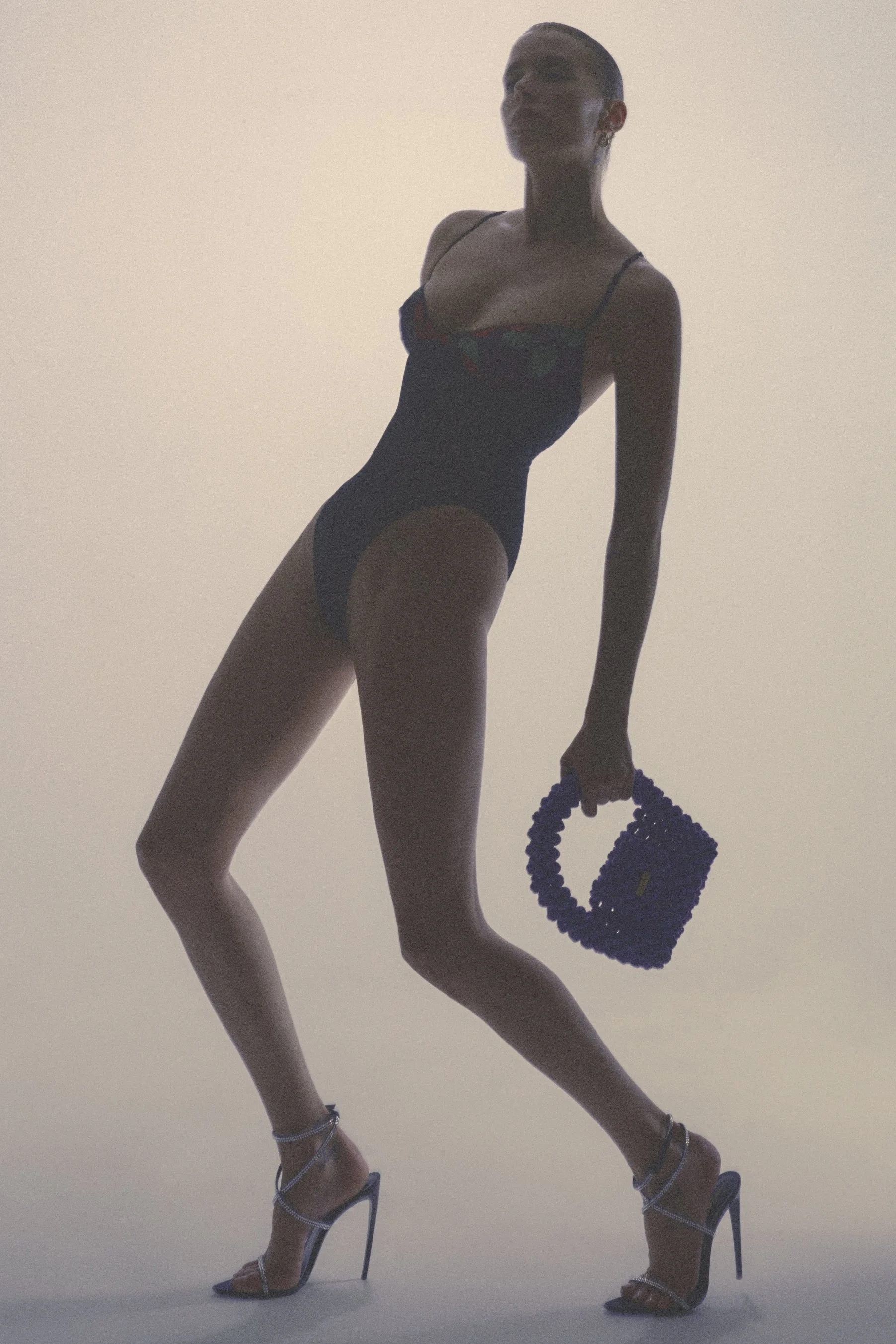 Backlit silhouette of a woman in black lingerie and heels holding a small beaded handbag.