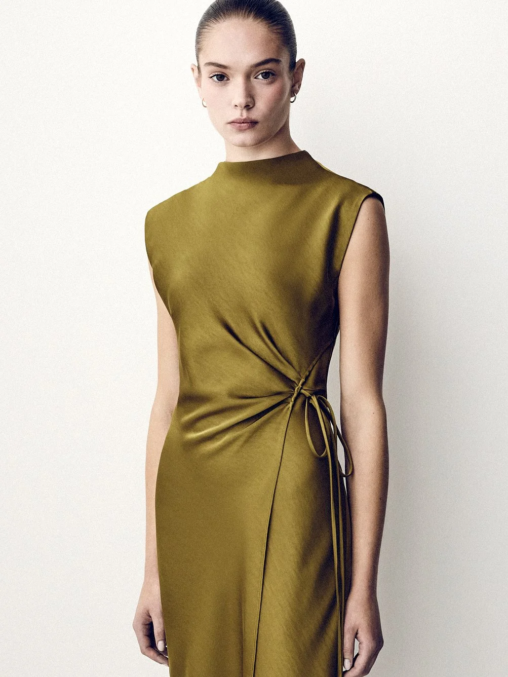 Woman wearing an olive sleeveless dress gathered and tied at the waist.