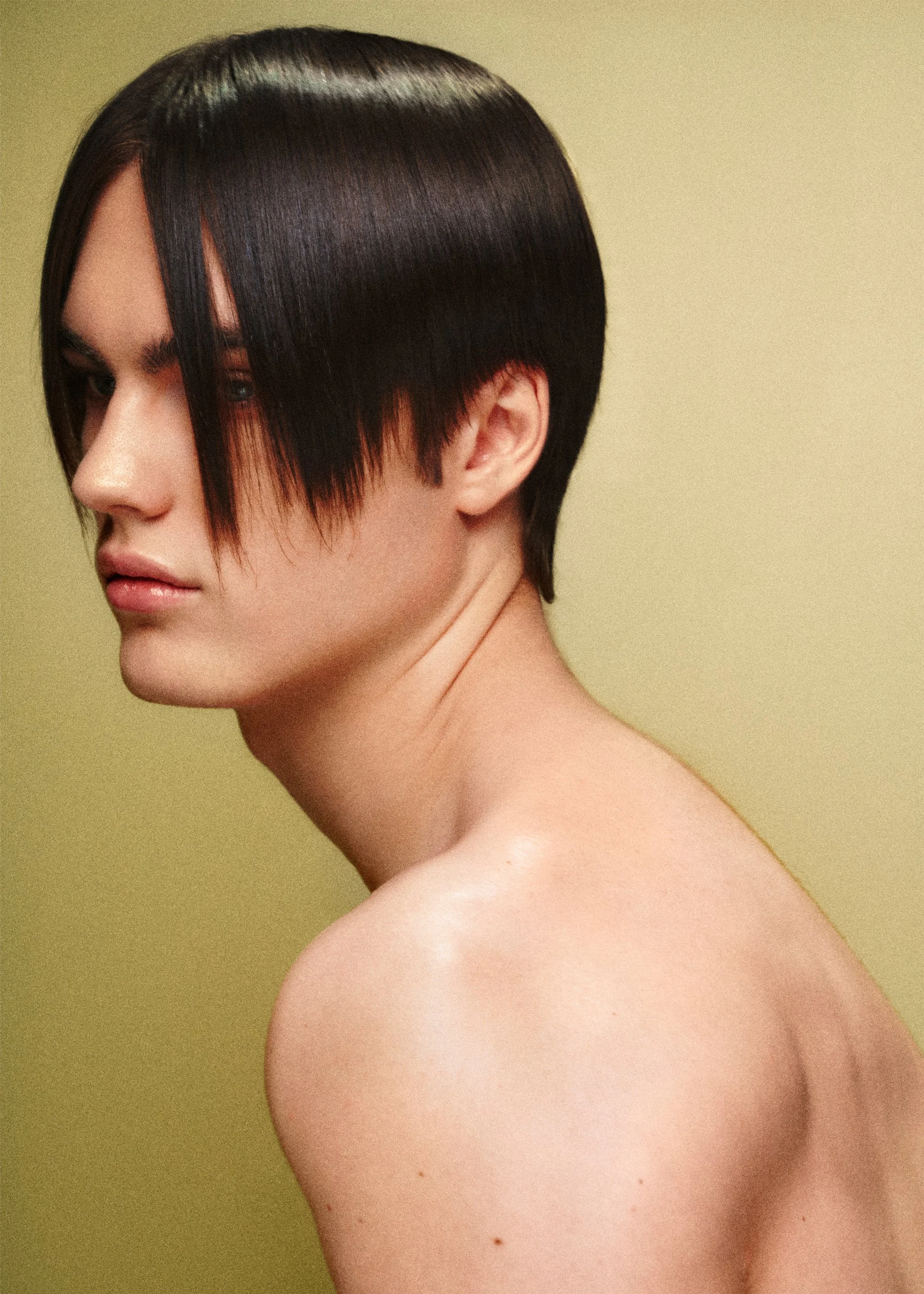Beauty portrait with a glossy black bob and long fringe against a pale yellow background.