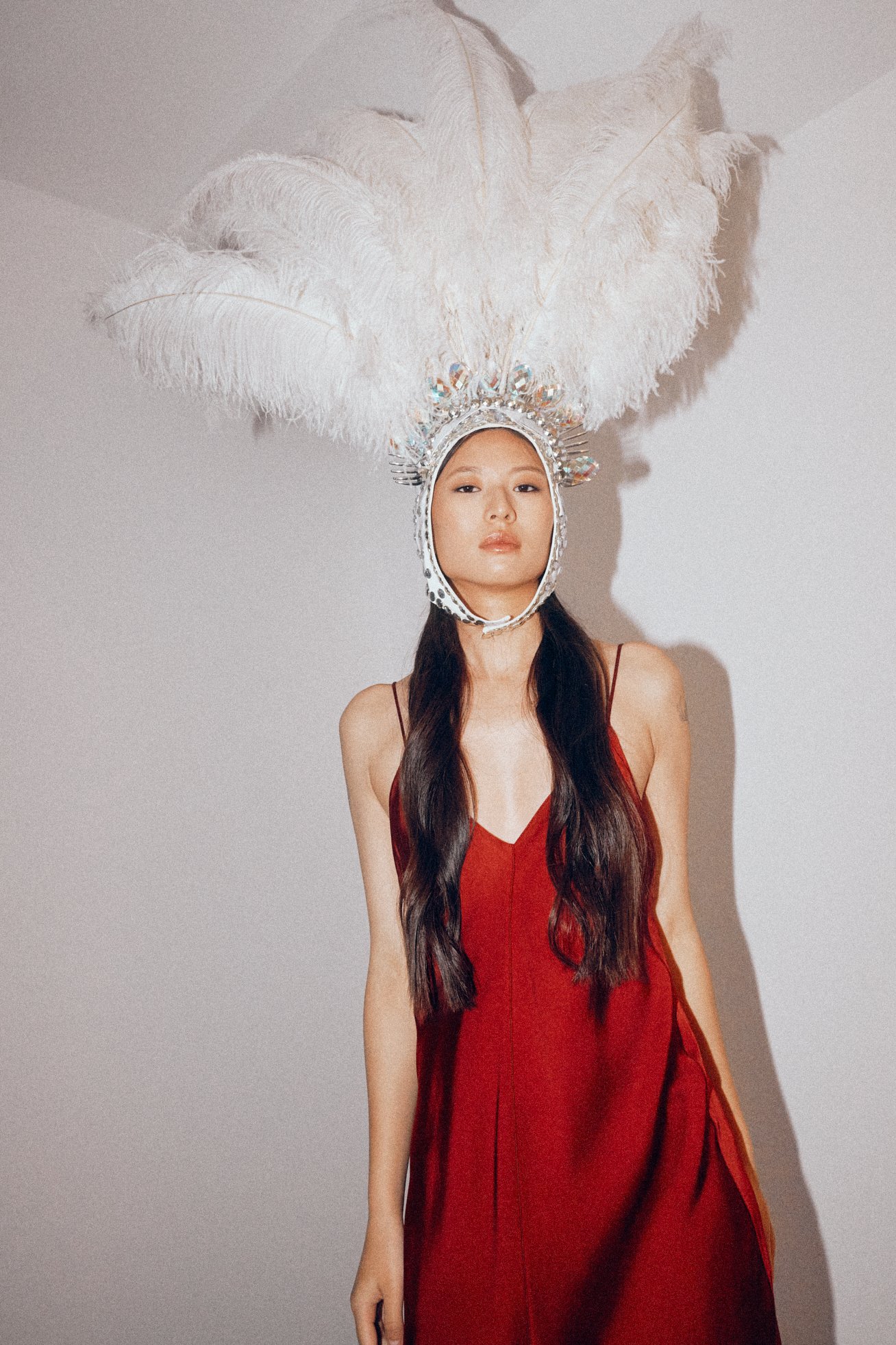 Woman in a red satin dress wearing a tall white feather headpiece.